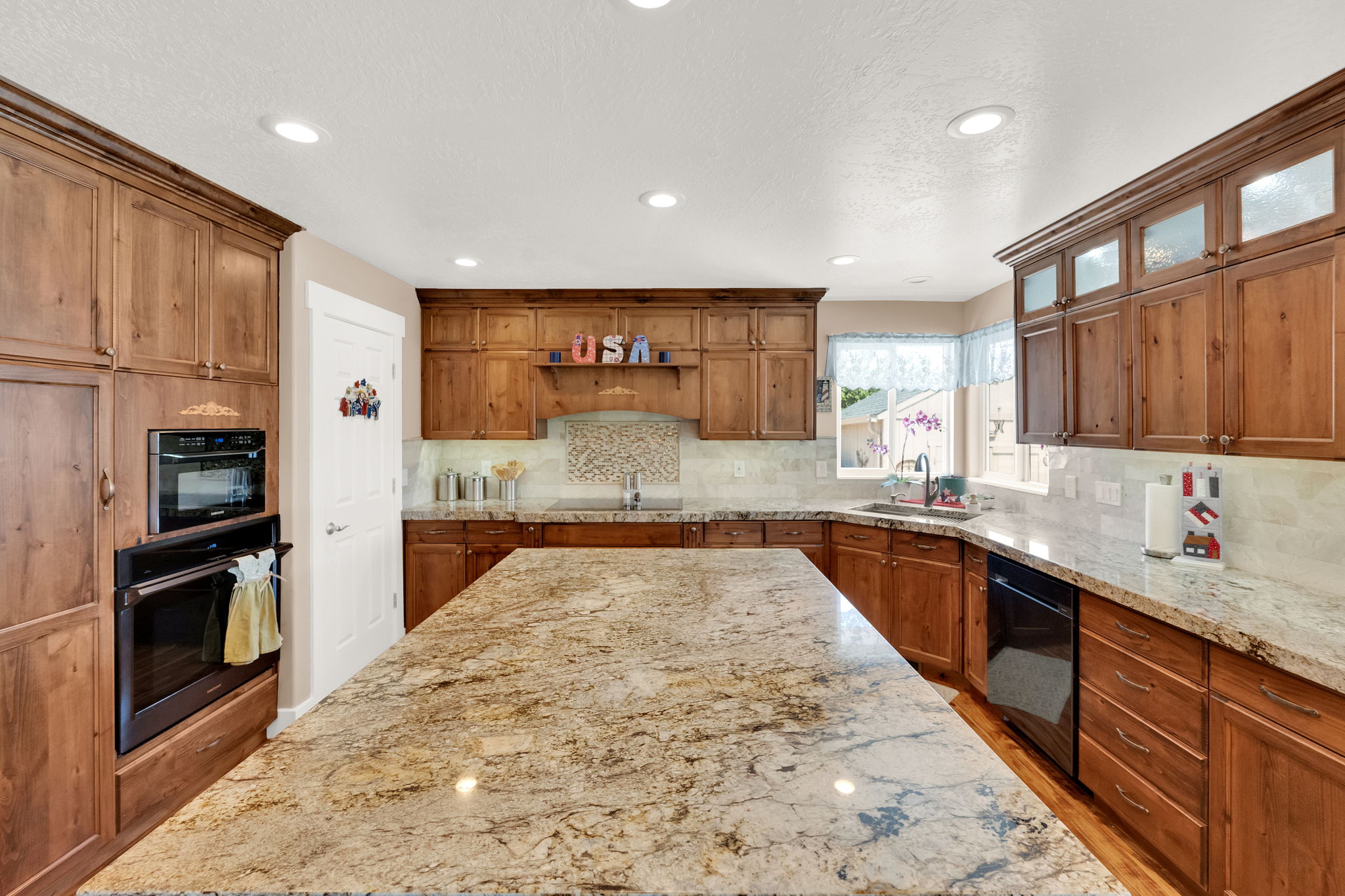 Spacious kitchen featuring a large granite-topped island, extensive wood cabinetry, stainless-steel double oven, and recessed lighting
