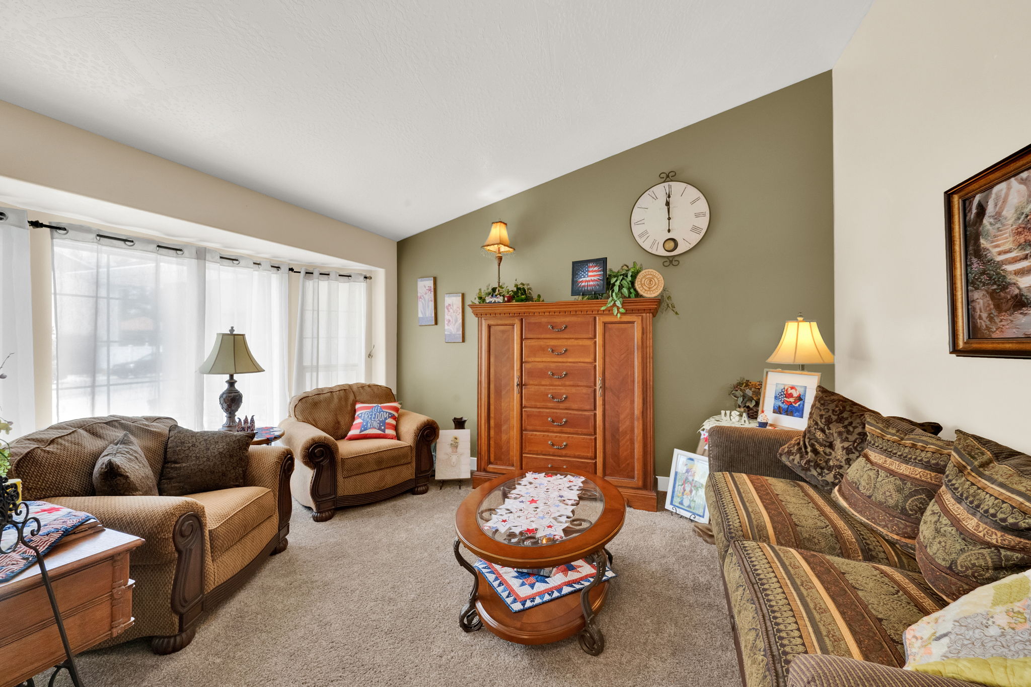 Living area featuring a bay window, vaulted ceiling, and carpet flooring