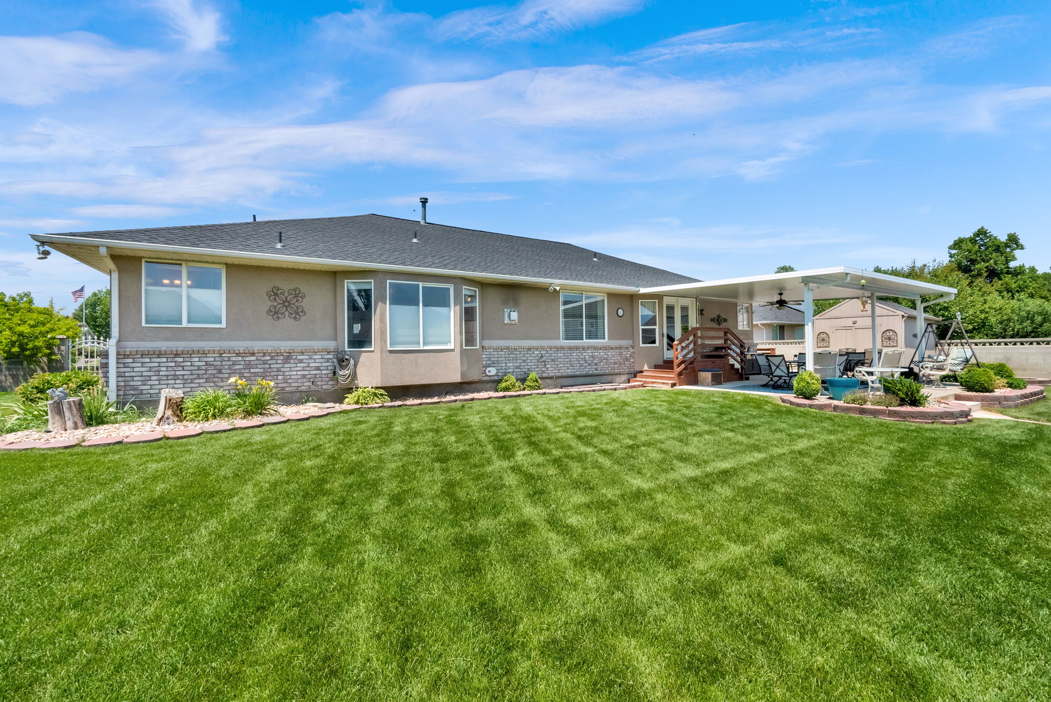 Expansive backyard featuring a manicured lawn, a covered patio structure, and a raised deck with wood railings