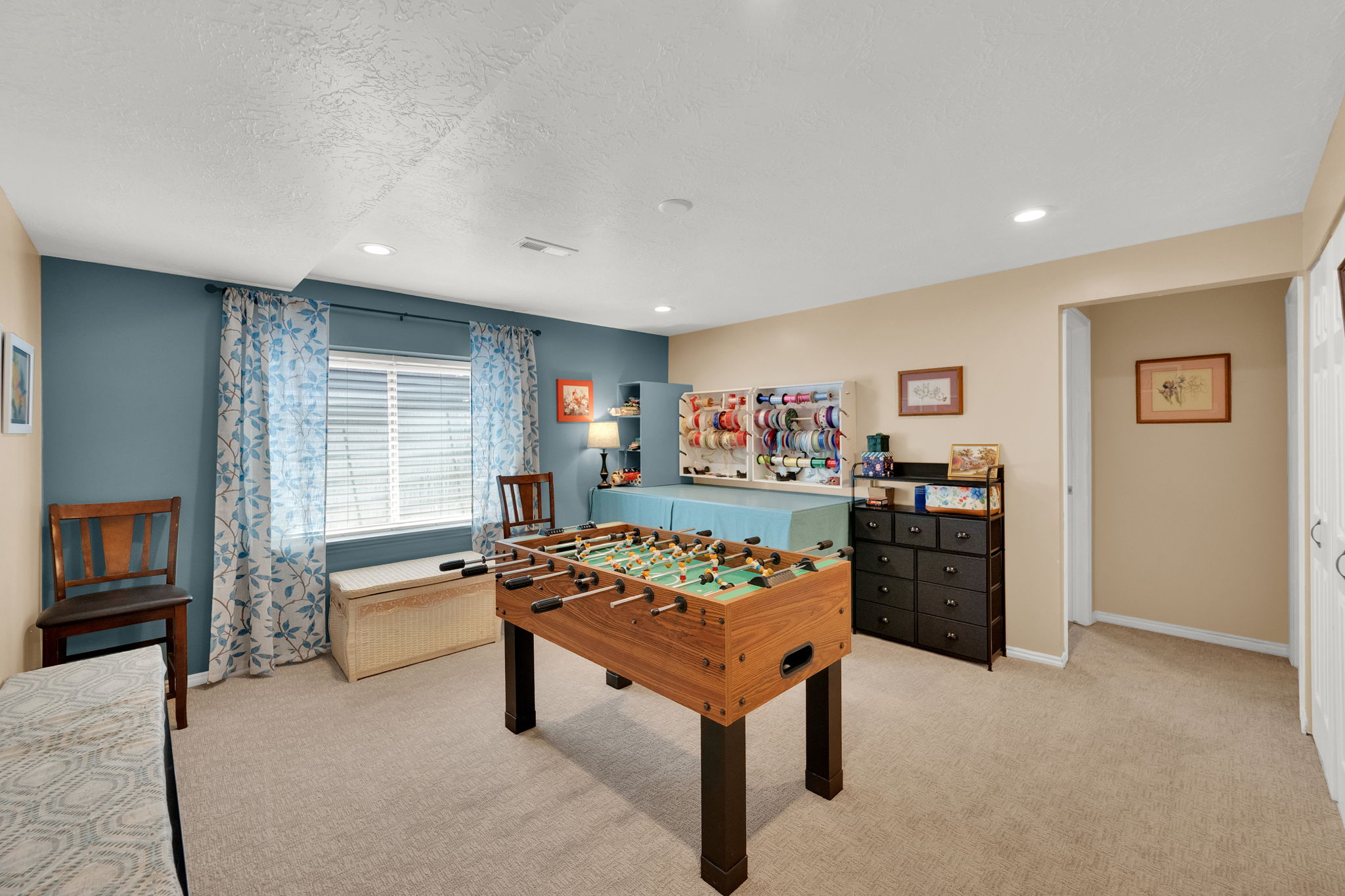 Spacious carpeted room featuring a window with horizontal blinds, recessed lighting, and a built-in shelving unit
