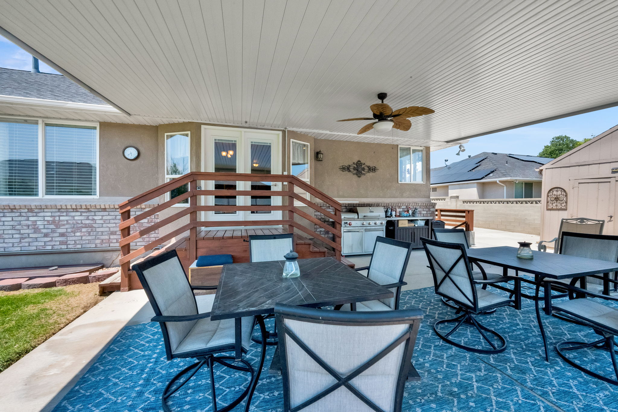 Covered patio featuring an outdoor kitchen, ceiling fan, and decorative wall sconce