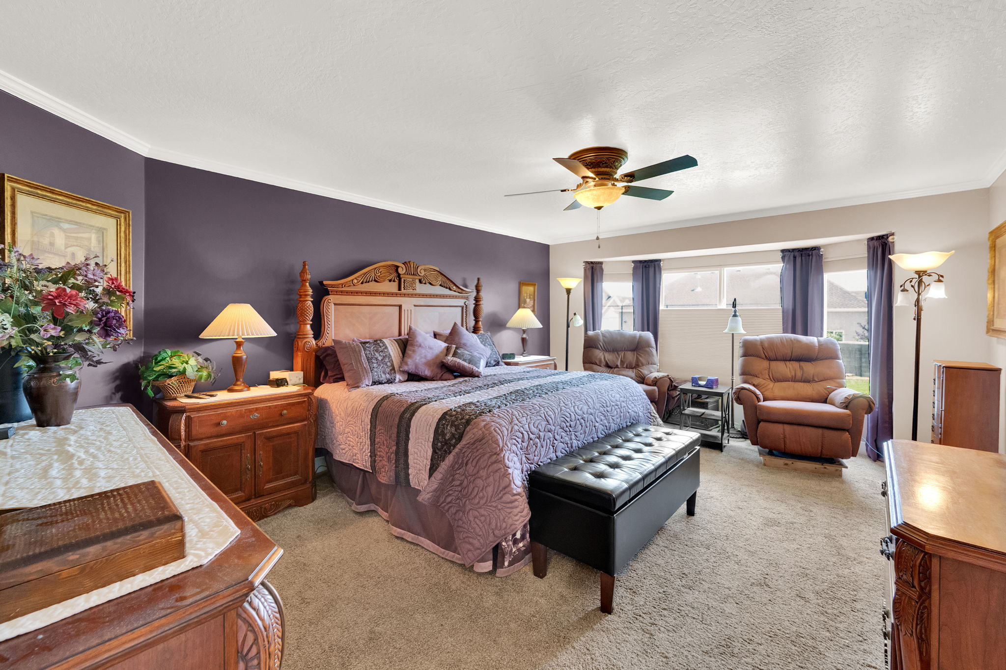 Spacious bedroom featuring neutral carpeting, a tray ceiling with a built-in ceiling fan, and crown molding