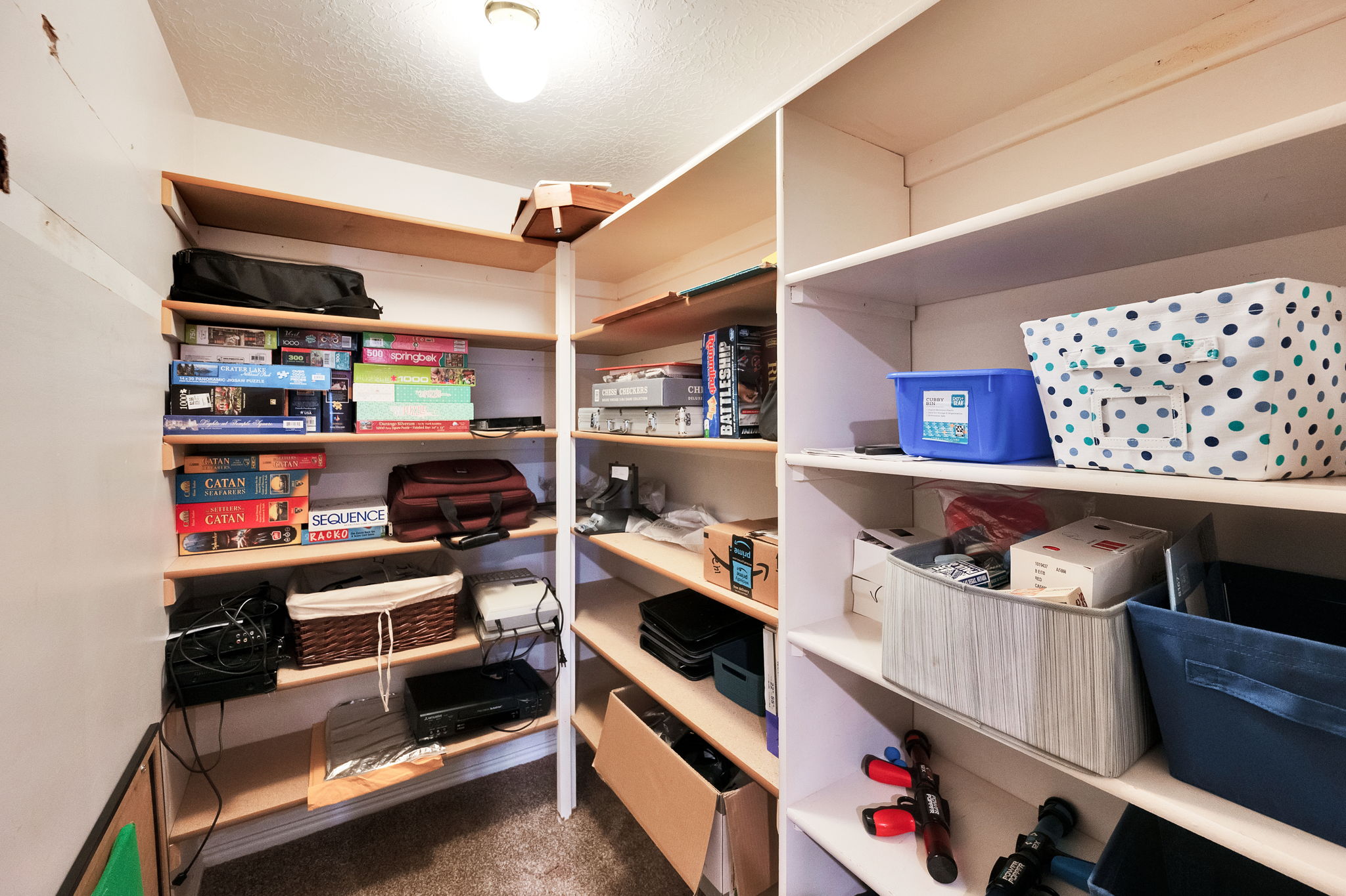 Generous storage closet featuring multiple tiers of built-in shelving, white painted walls, and overhead lighting