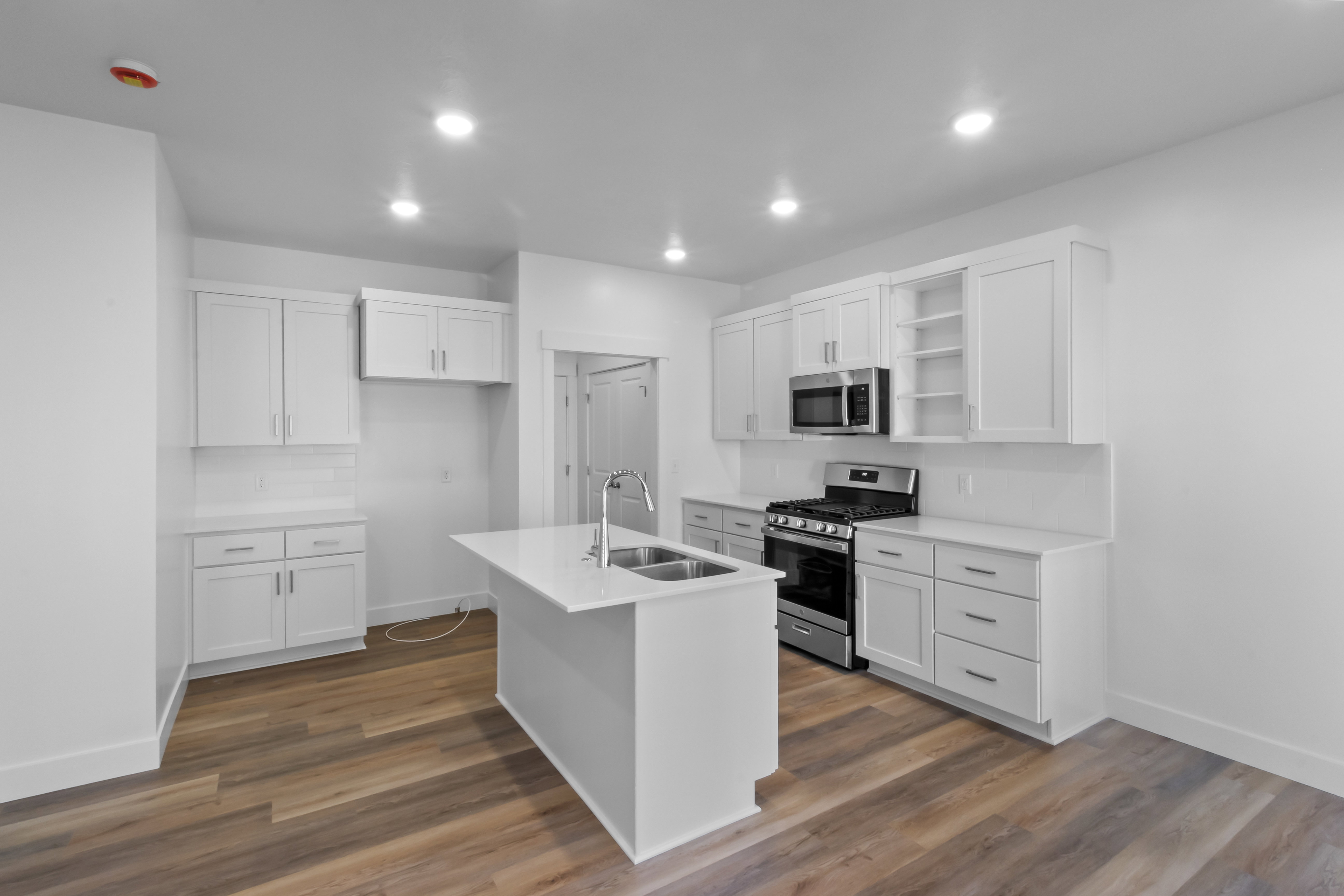Modern kitchen featuring an island with an undermount sink, white cabinetry, stainless steel appliances, wood-finish flooring, and recessed lighting