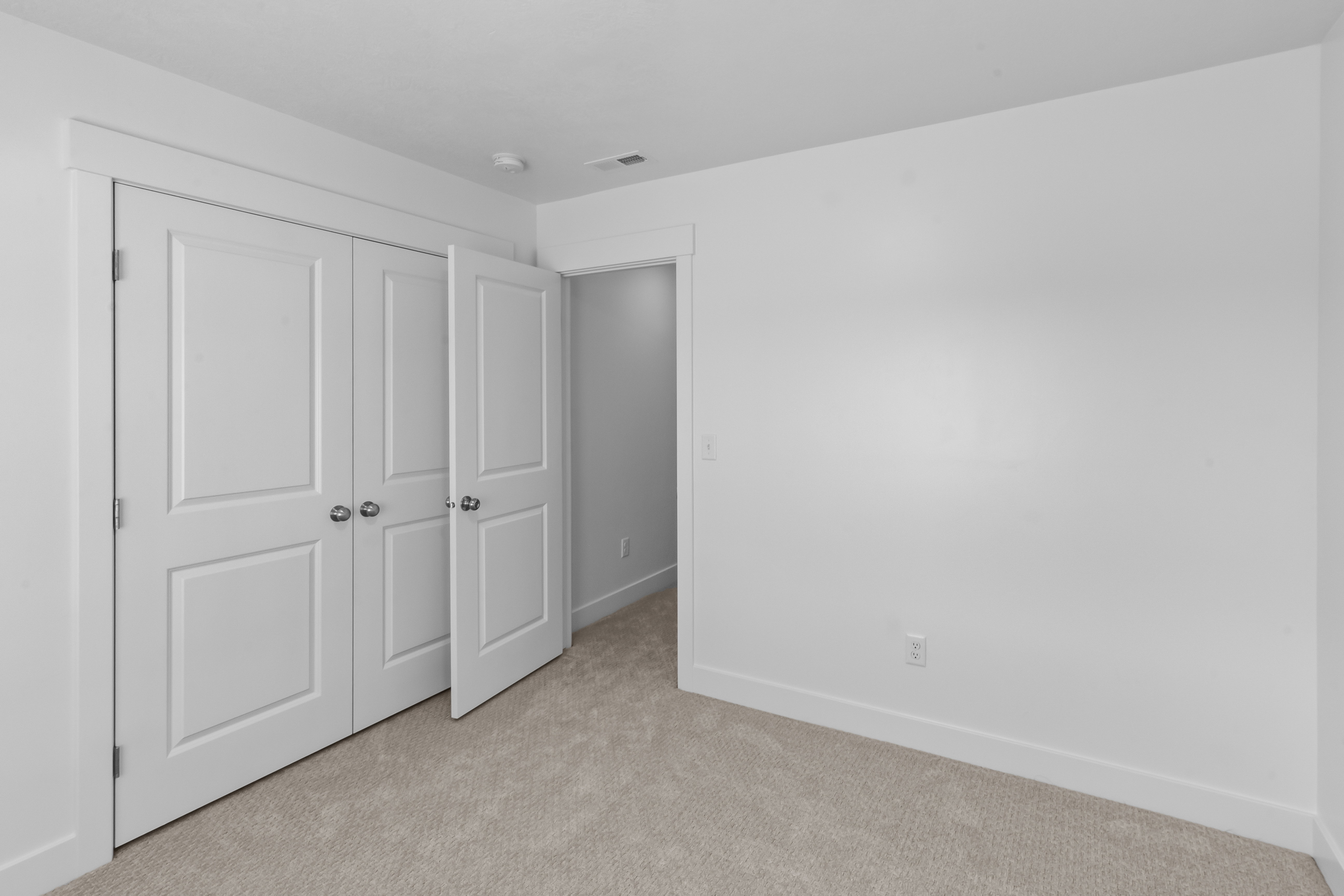 Bedroom featuring neutral carpeting, white walls, and a double-door closet with paneling