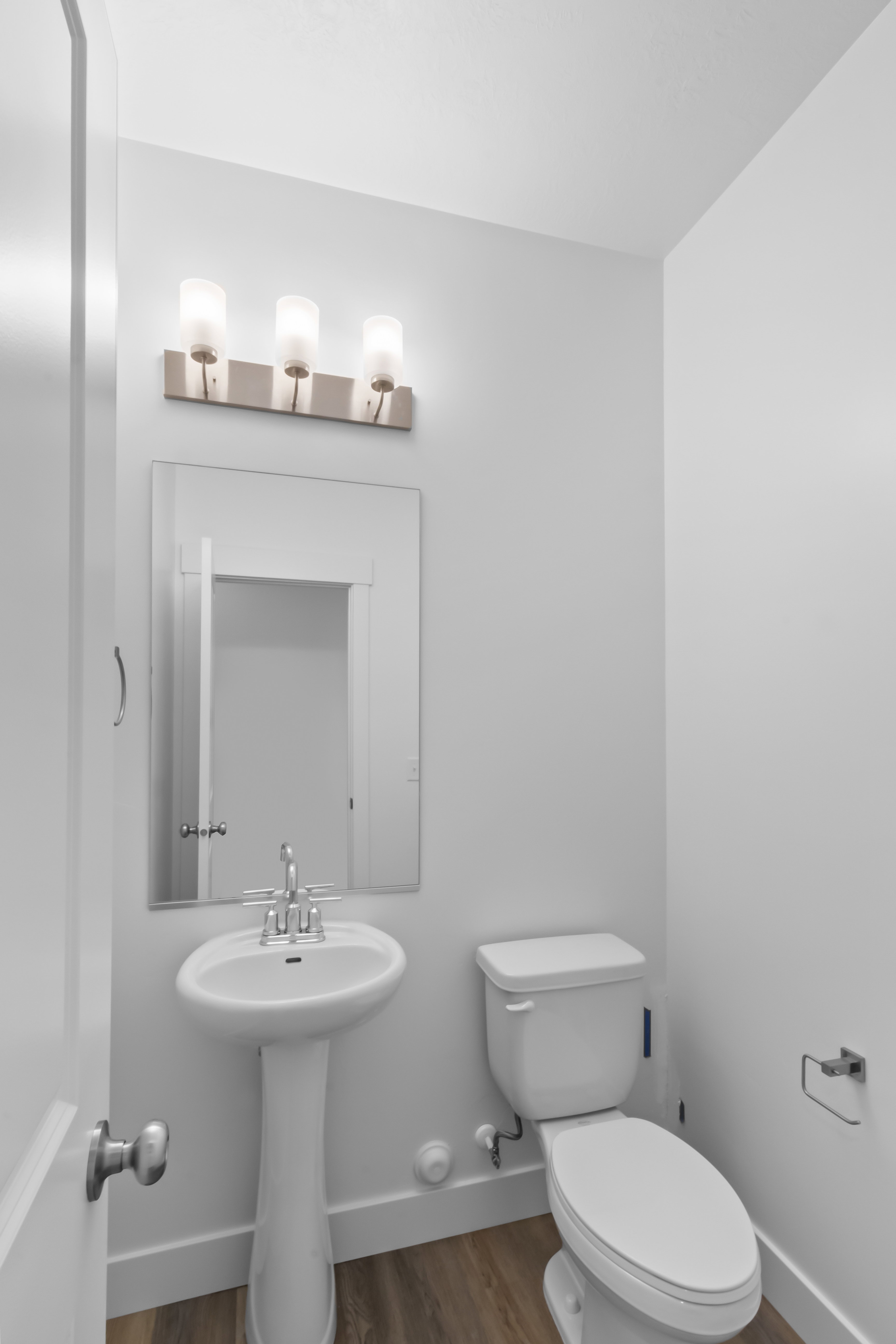 Pedestal sink with chrome faucet, a white toilet, and a rectangular mirror