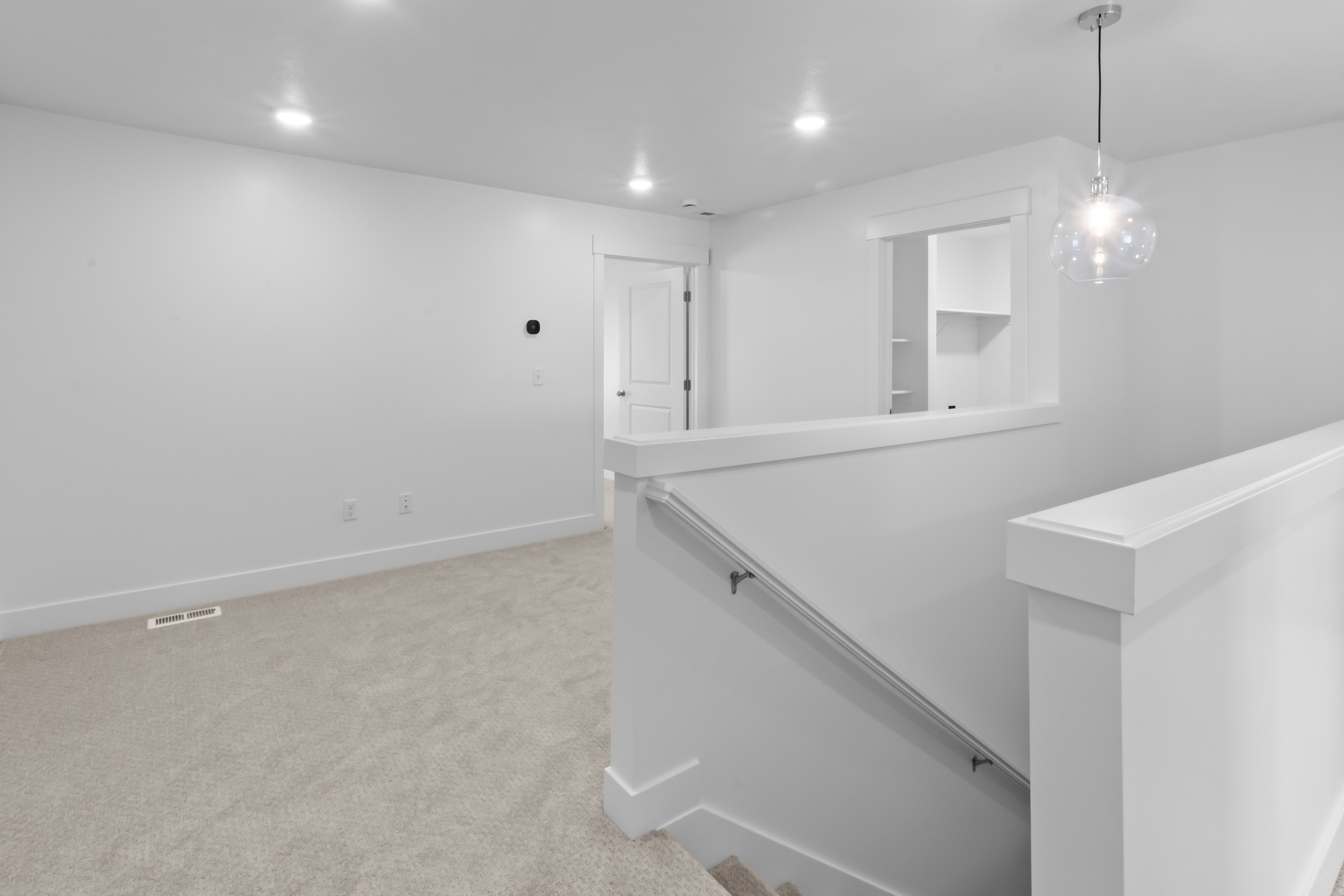 Carpeted upper-level landing with recessed lighting, a modern glass orb pendant light, a white painted railing, and a framed opening revealing built-in shelving