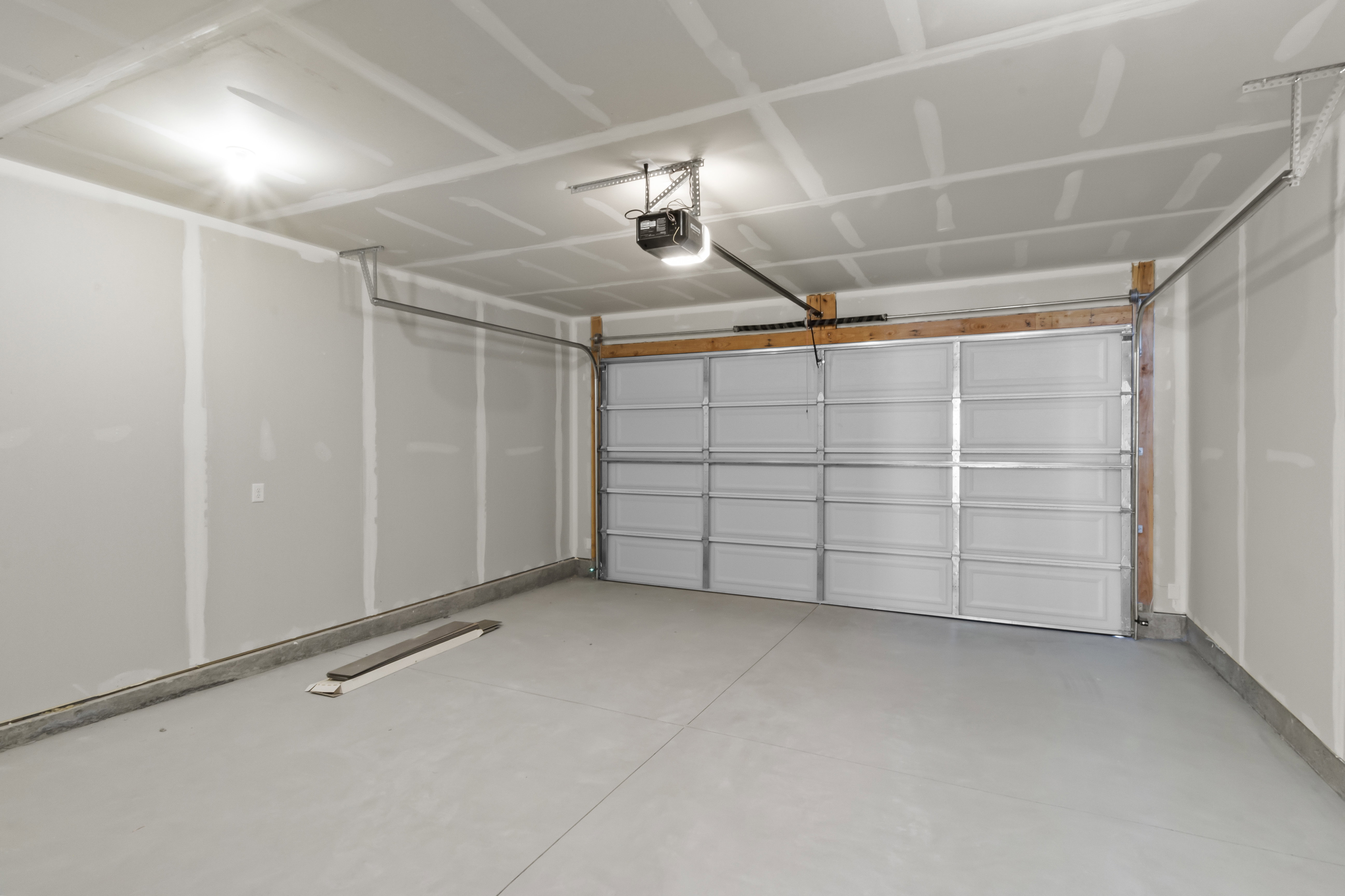 Spacious garage featuring a sectional garage door, exposed wood framing, and light-colored flooring