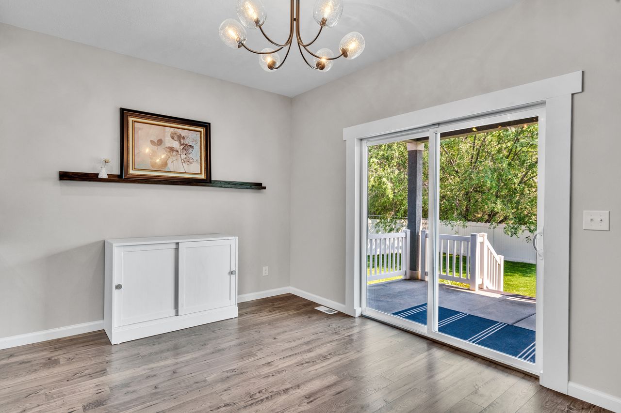 Sliding glass patio door with white trim, wood-finish flooring, and a contemporary chandelier