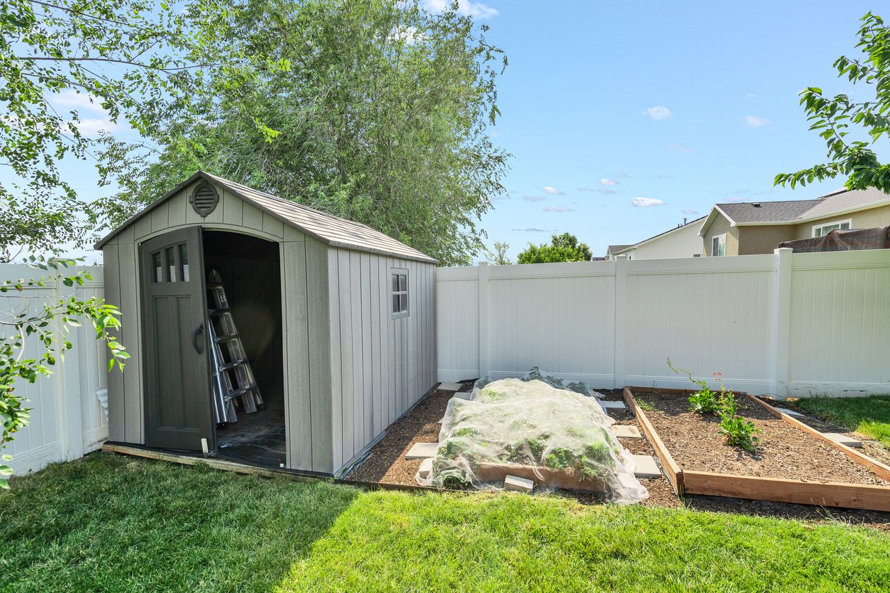 Backyard featuring a shed with a single arched door and side window, white vinyl fencing, and two raised garden beds