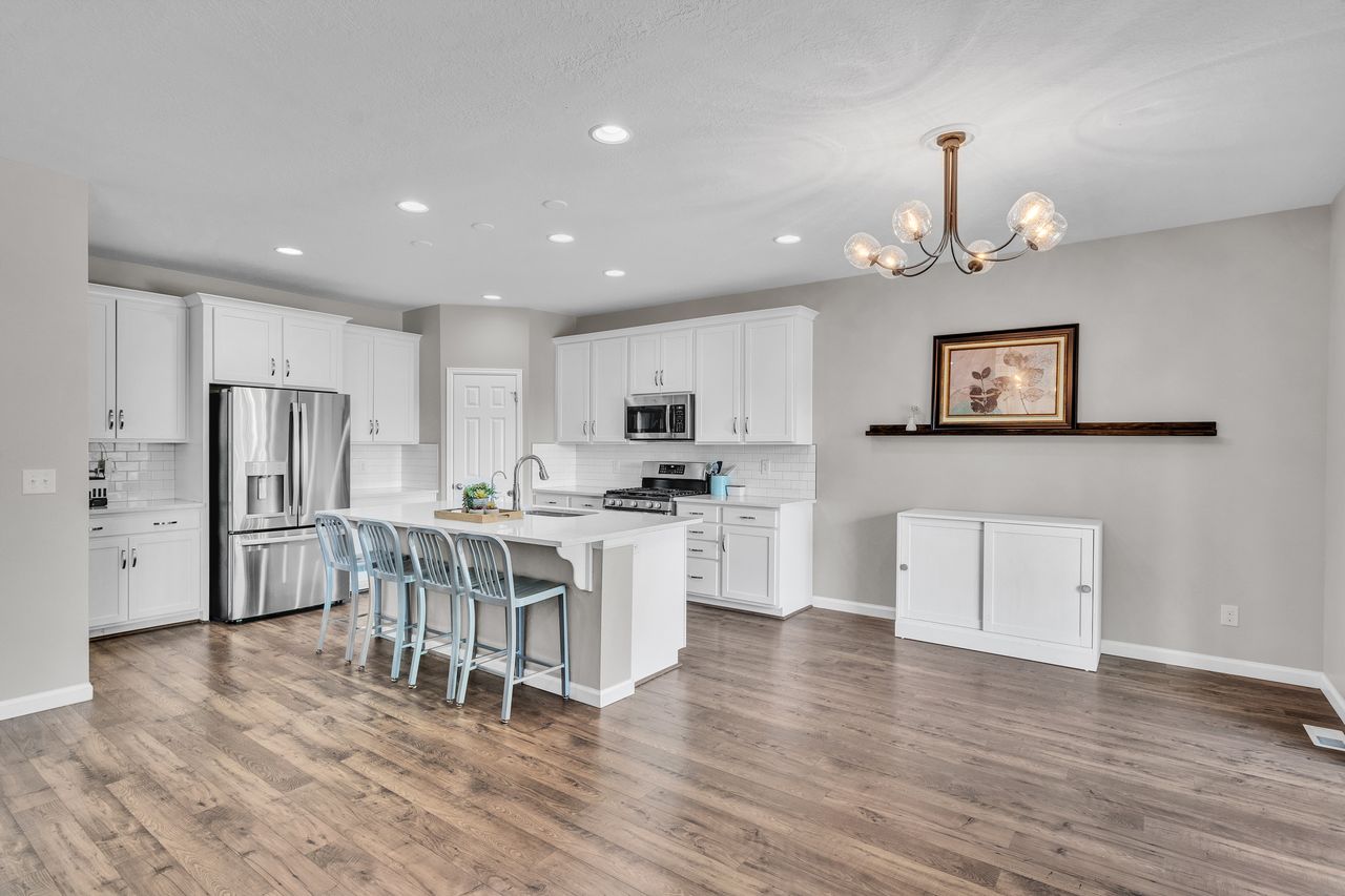 Kitchen featuring a central island with seating, stainless steel appliances, white cabinetry, wood-finish flooring, and recessed lighting