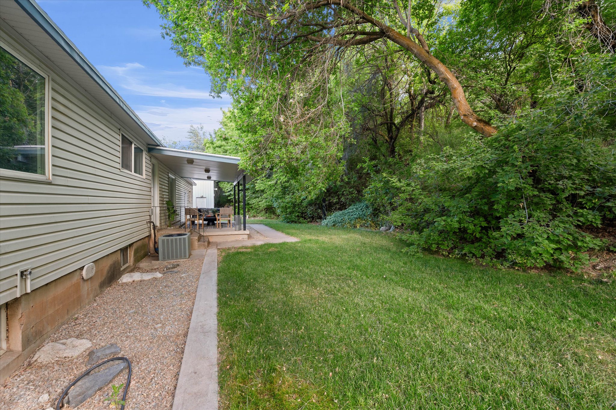Expansive green lawn with a covered patio, featuring a gravel perimeter and dense mature trees providing a natural backdrop