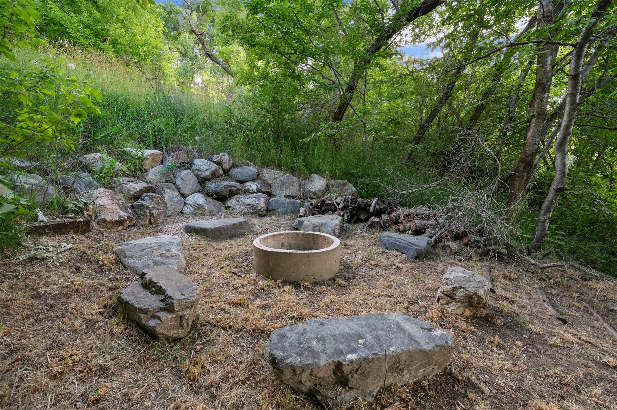 Outdoor fire pit area featuring a concrete fire ring, surrounding natural stone seating, and a rock retaining wall