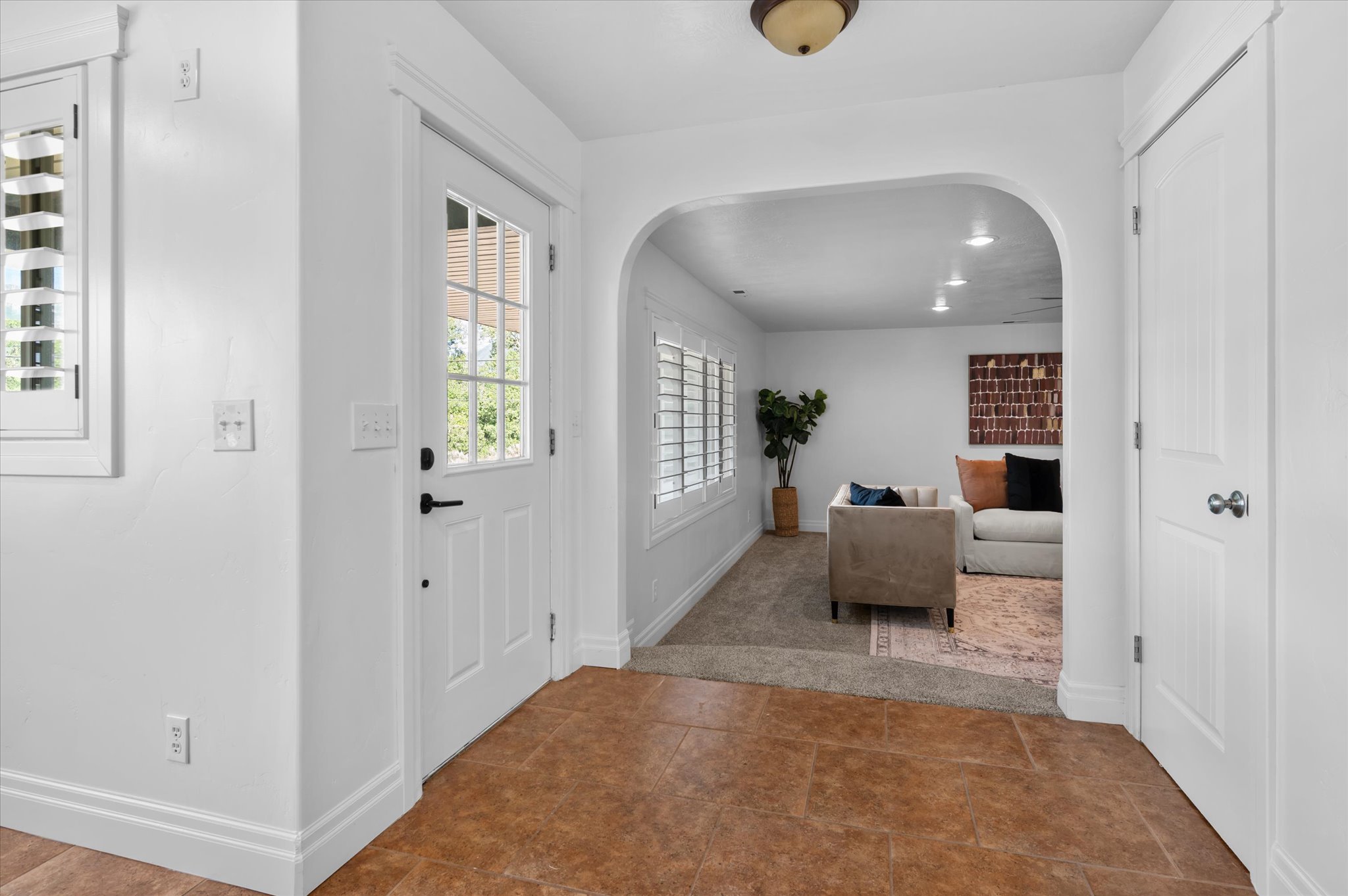 Foyer with tile flooring, a white glass-paneled entry door, and a white plantation-shuttered window