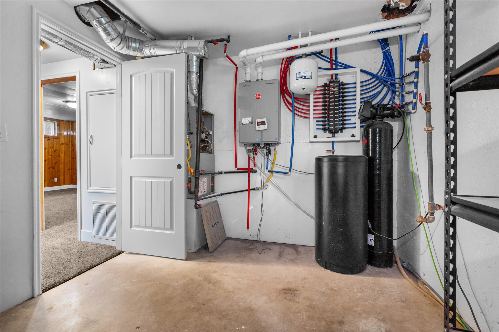 Mechanical room featuring a tankless water heater, water treatment system, and HVAC unit with exposed ductwork