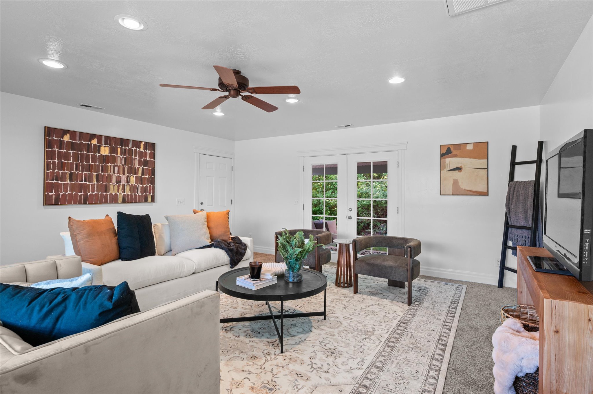 Recessed lighting illuminates this bright living space featuring a ceiling fan, light-toned walls, and a combination of carpet and an area rug