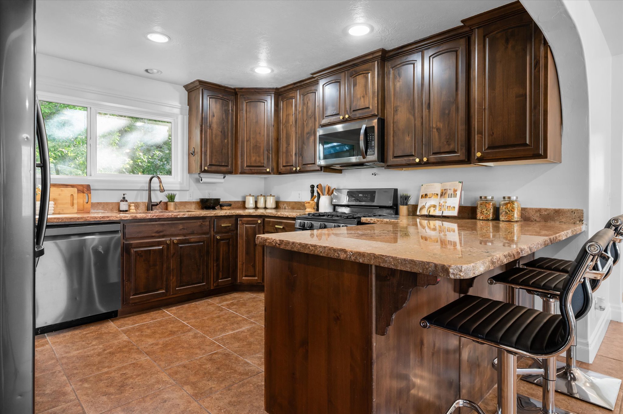 Kitchen featuring rich wood cabinetry, granite countertops, stainless steel appliances, recessed lighting, and tile flooring