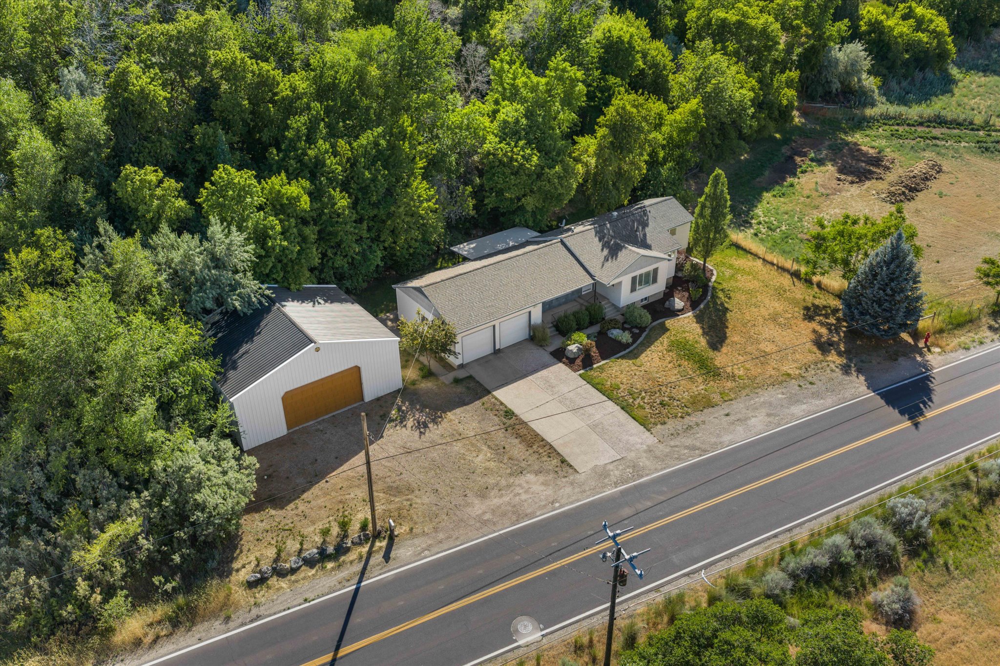 Ranch-style residence featuring an attached two-car garage, separate detached garage, paved driveway, mature landscaping, and surrounding wooded areas