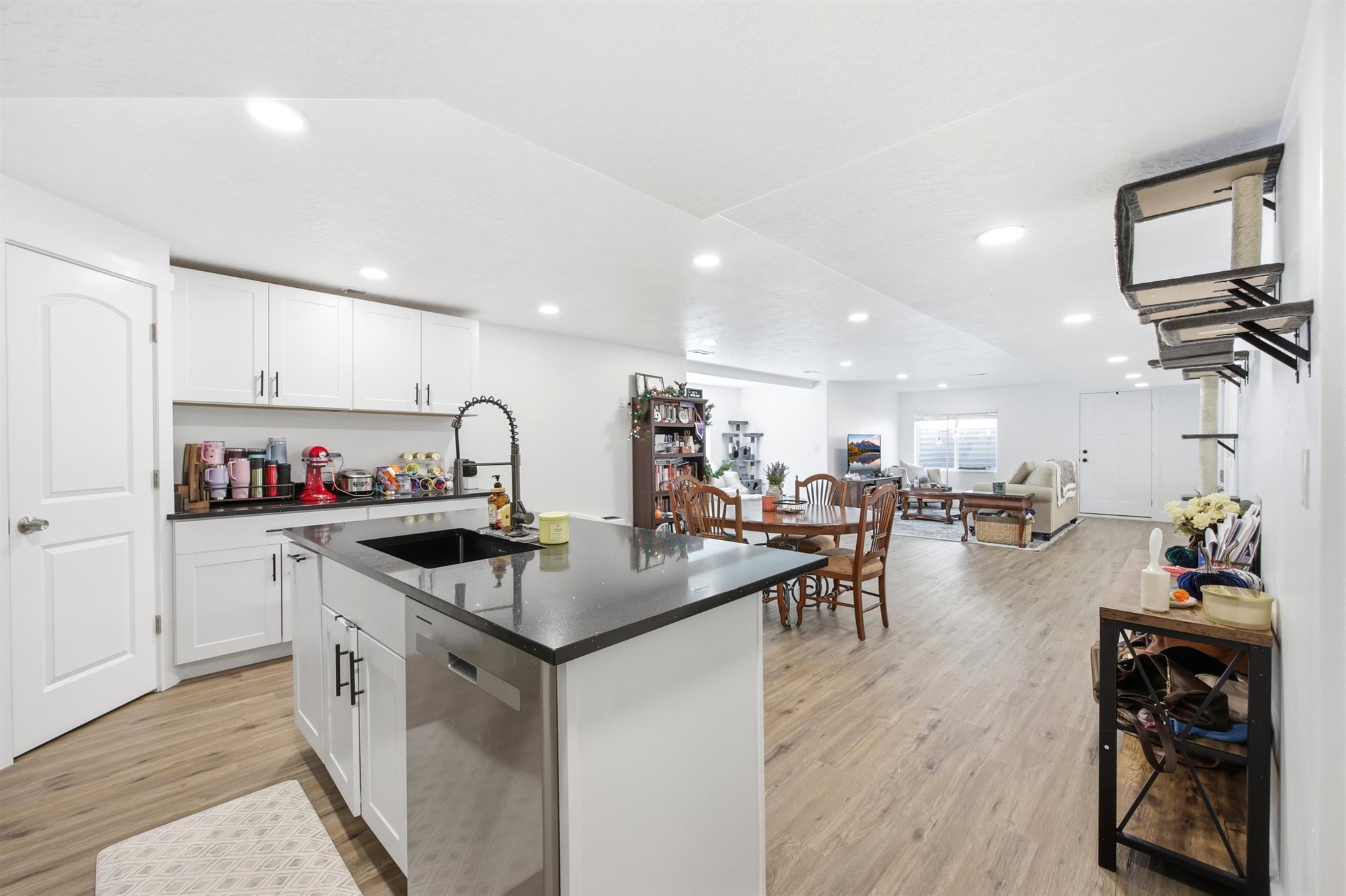 Open-concept living space featuring a central kitchen island with a dark sink and faucet, white cabinetry, dark countertops, and wood-finish flooring throughout