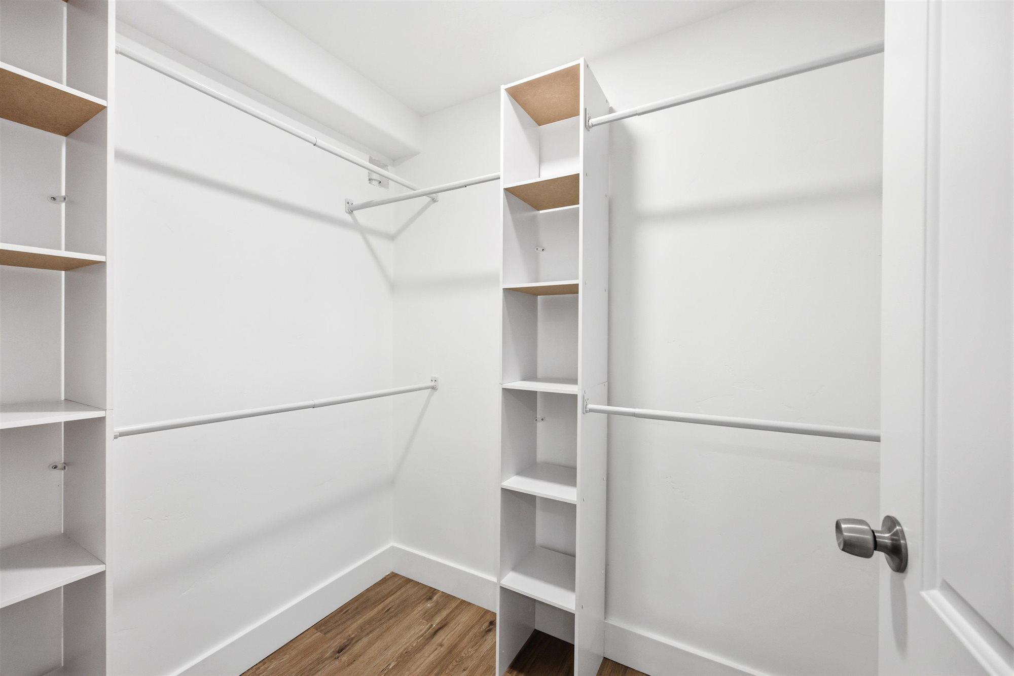 Walk-in closet featuring built-in shelving, multiple hanging rods, white walls, white baseboards, and wood-finish flooring