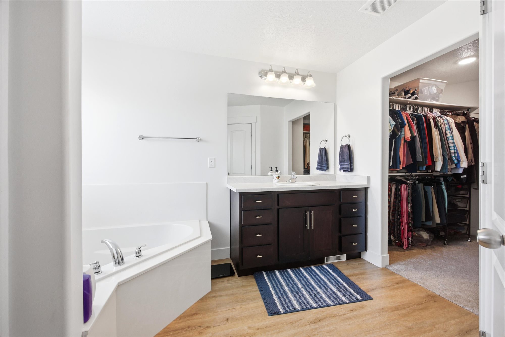 Spacious bathroom featuring a corner soaking tub, wood-finish flooring, and a dark wood vanity with white countertop
