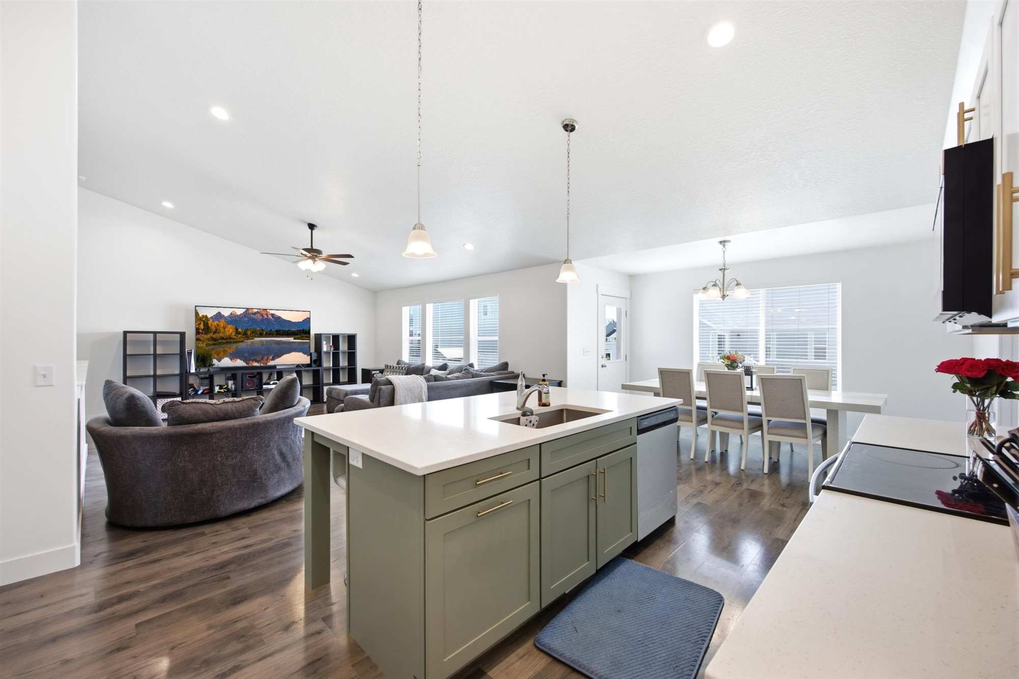 Open-concept living space featuring wood-finish flooring, a kitchen island with light green cabinetry and a white countertop, recessed lighting, and a dining area with a chandelier