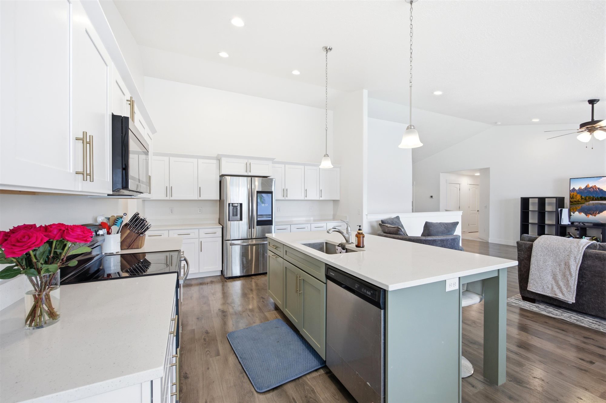 Bright kitchen featuring white shaker cabinetry, stainless steel appliances, and a central island with a sink and pendant lighting