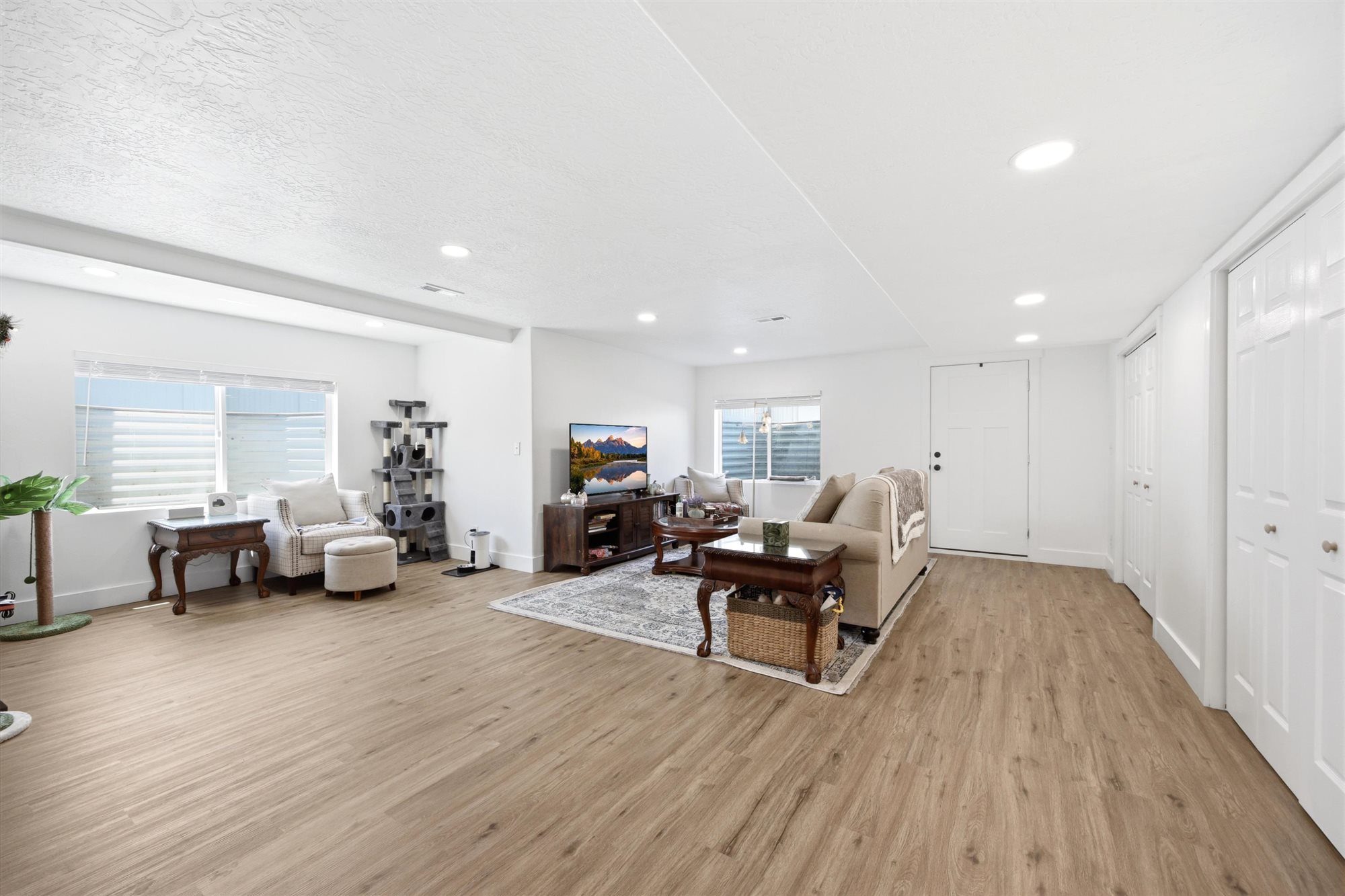 Spacious living area featuring light wood-finish flooring, recessed lighting, and bright white walls