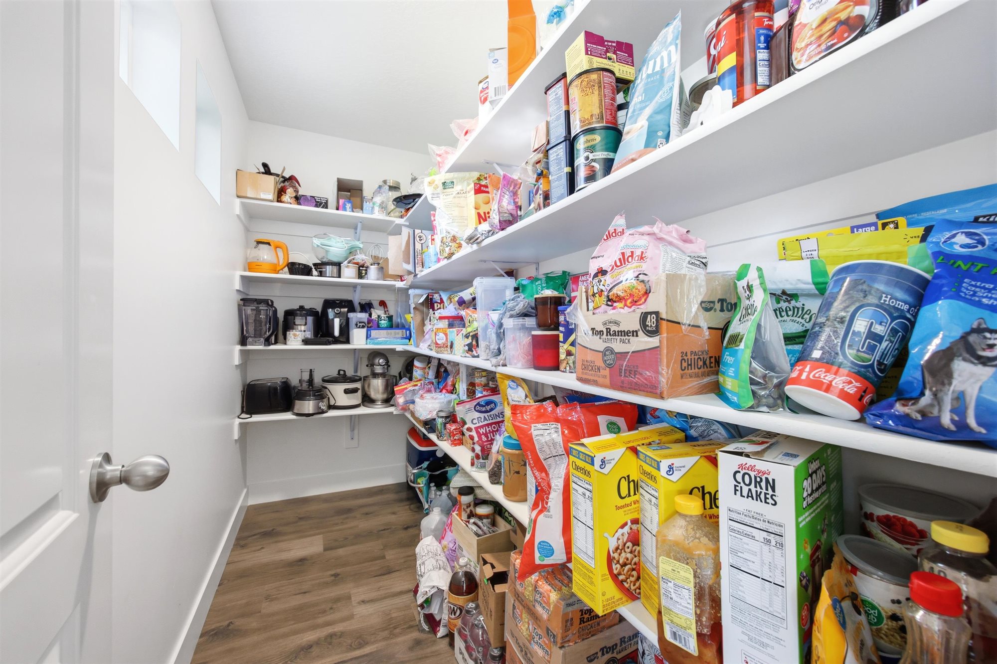 Walk-in pantry featuring extensive white shelving, wood-finish flooring, and white walls