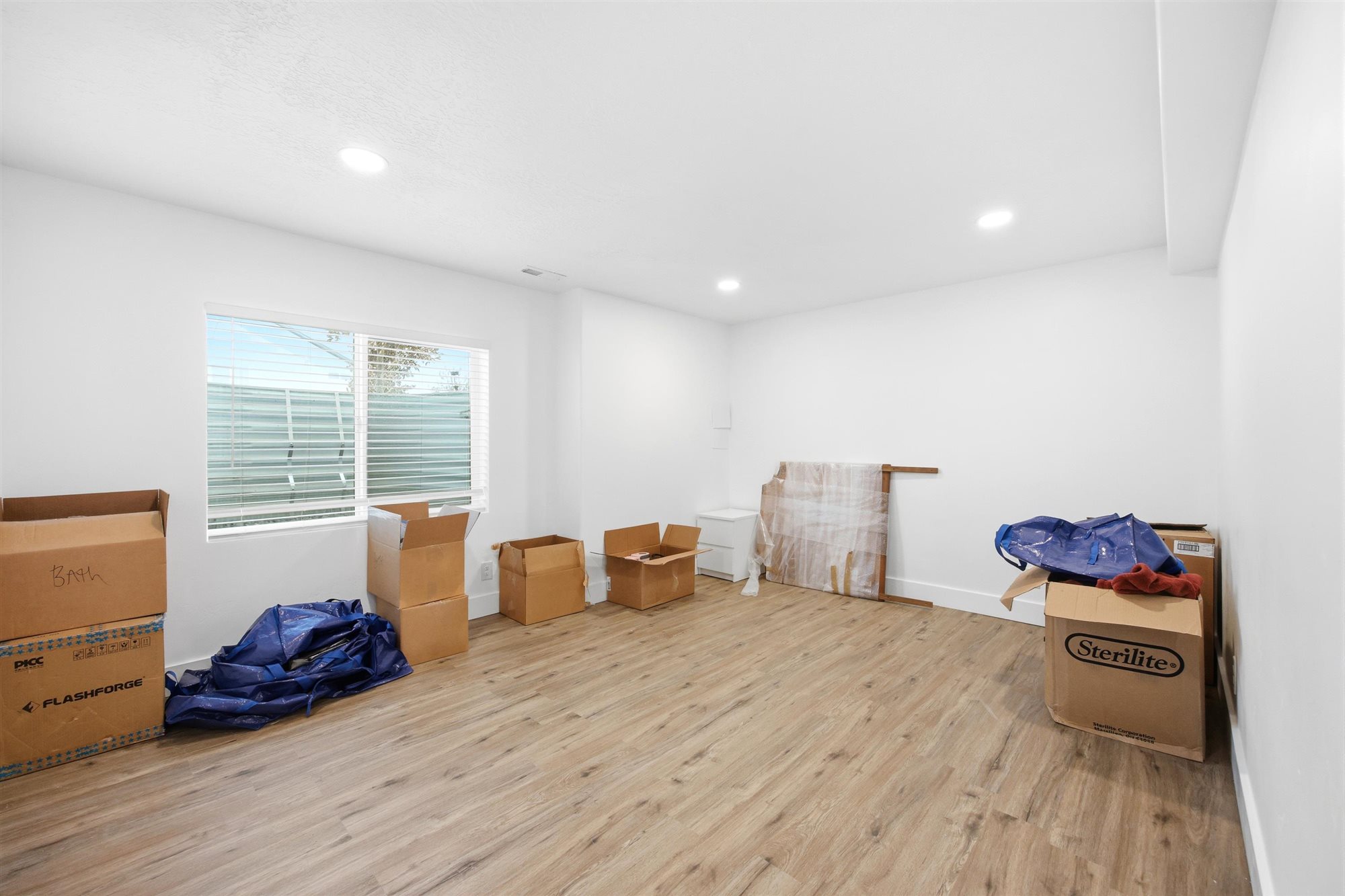 Bright room featuring wood-finish flooring, recessed lighting, white walls, and a large window with horizontal blinds