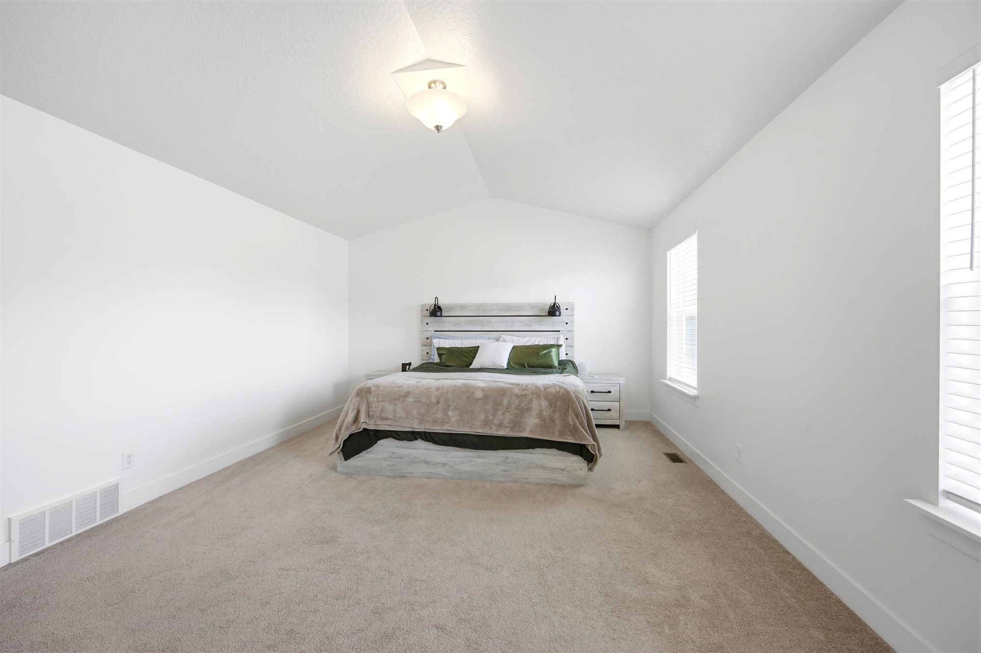 Spacious room featuring vaulted ceilings, light-toned carpeting, multiple windows with blinds, and white wall finishes