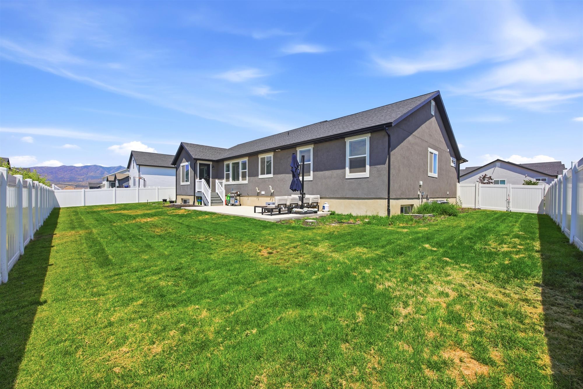 Expansive fenced backyard featuring a concrete patio, white vinyl fencing, and a stucco exterior