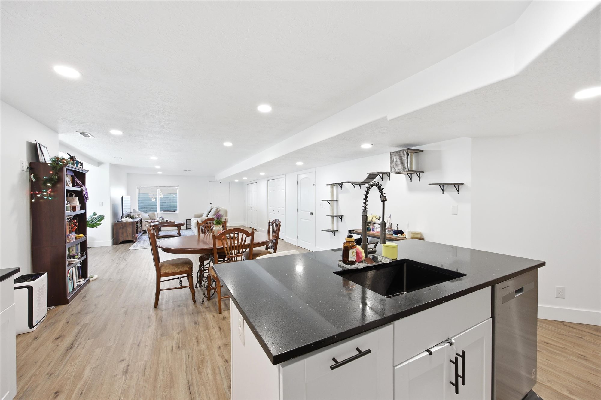 Spacious open-concept living area featuring a kitchen island with black countertop and integrated sink, recessed lighting, wood-finish flooring, and white walls