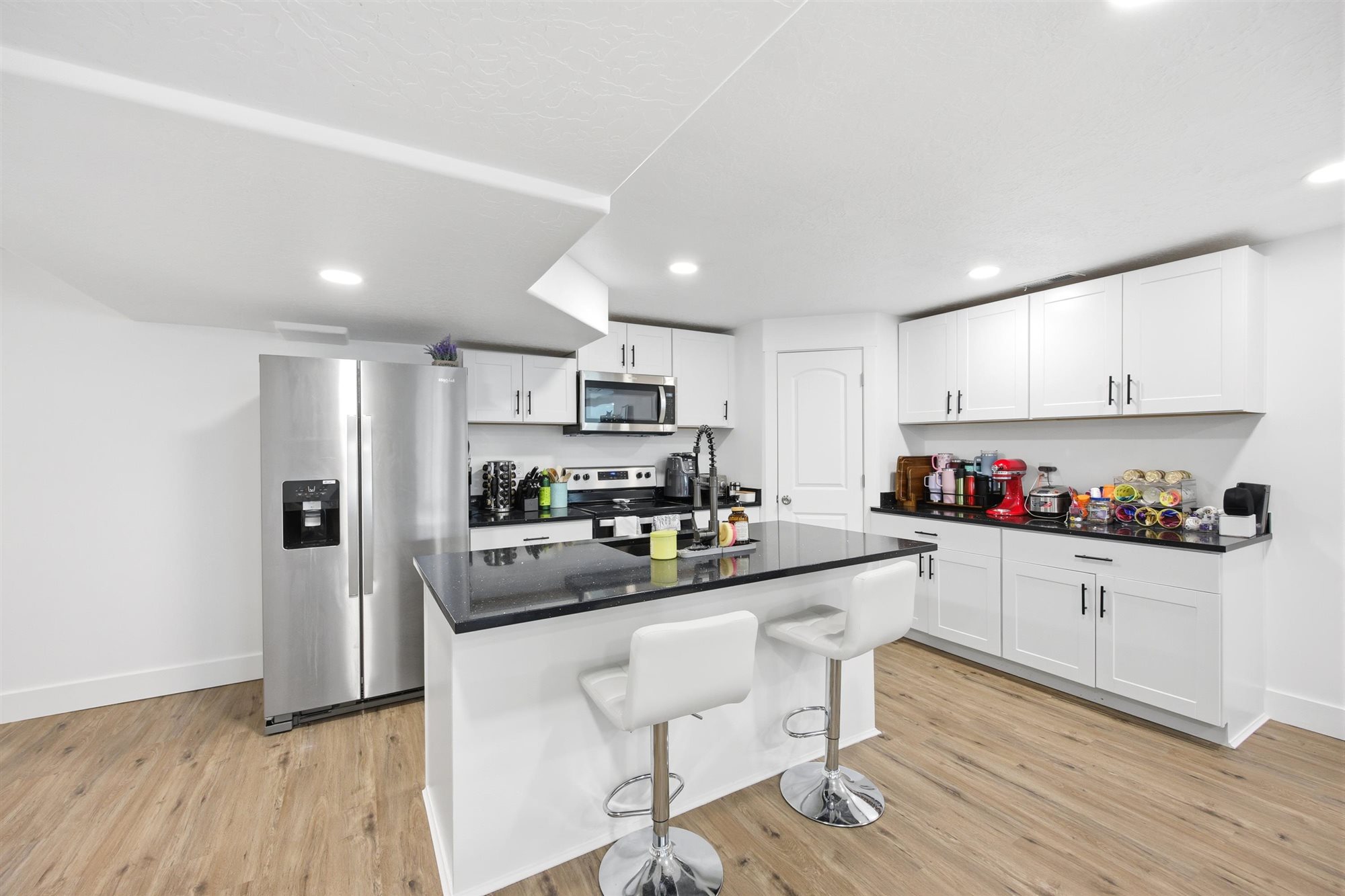 Kitchen featuring wood-finish flooring, white cabinetry, dark countertops, a stainless steel refrigerator, and recessed lighting