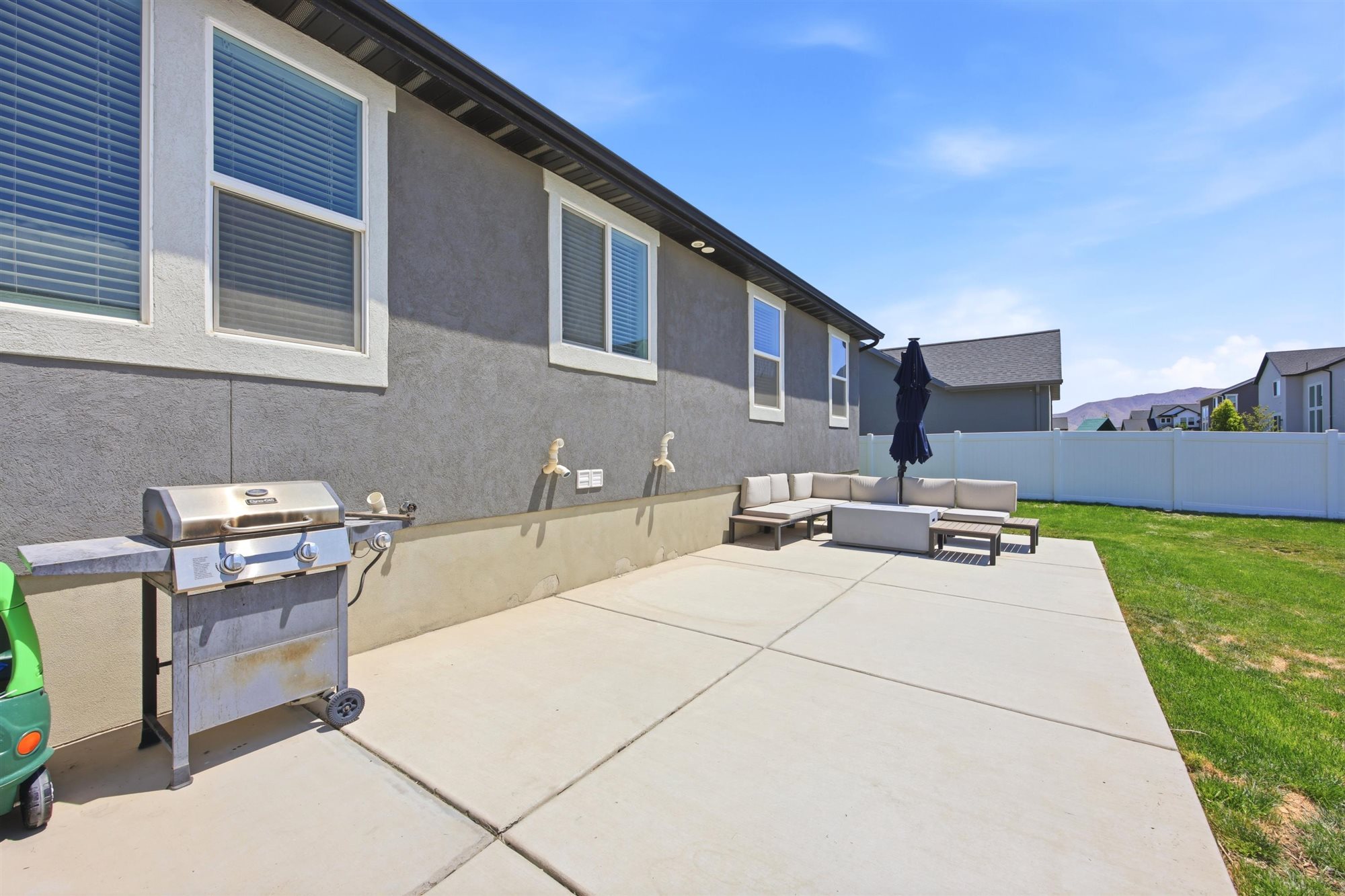 Paved concrete patio and green lawn area bordered by a white privacy fence