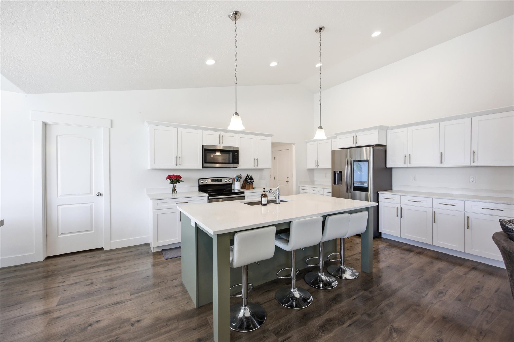 Spacious kitchen featuring an expansive island with seating, white shaker cabinetry, stainless steel appliances, and vaulted ceilings with recessed lighting
