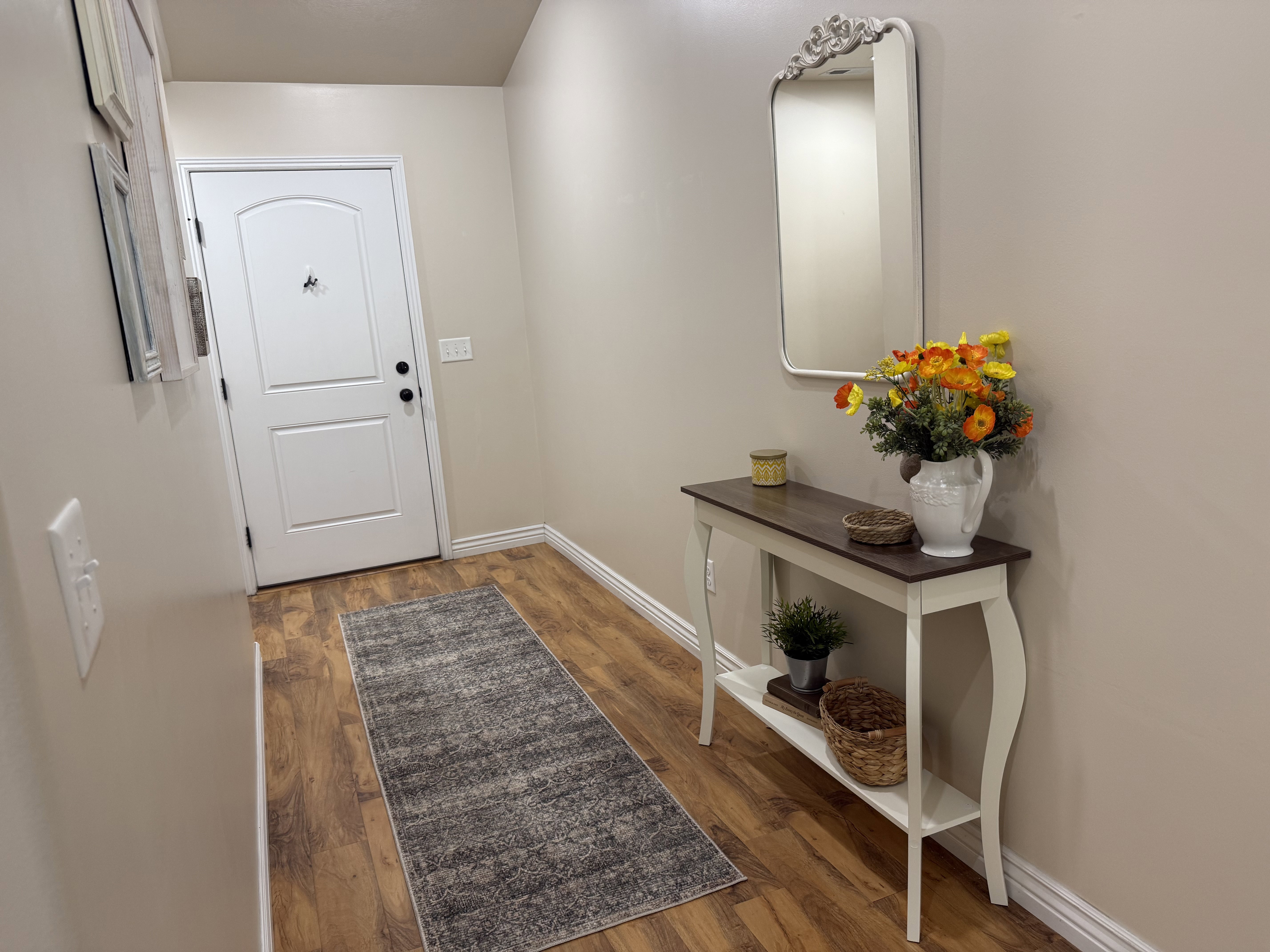 Spacious entryway featuring wood-finish flooring, a white paneled door, and a decorative wall mirror with an ornate frame