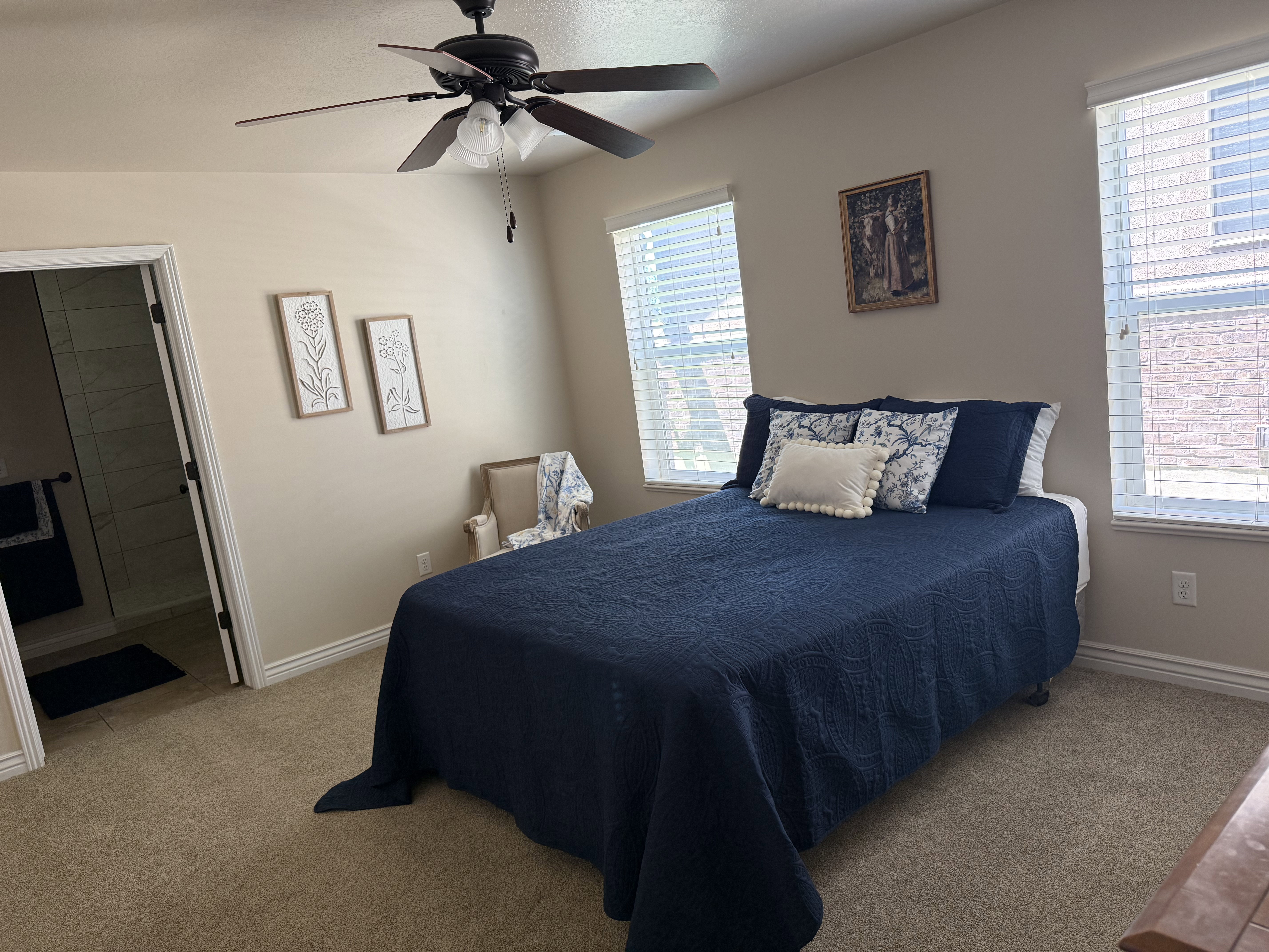 Carpeted room featuring a ceiling fan, two windows with blinds, and an open doorway revealing a tiled bathroom