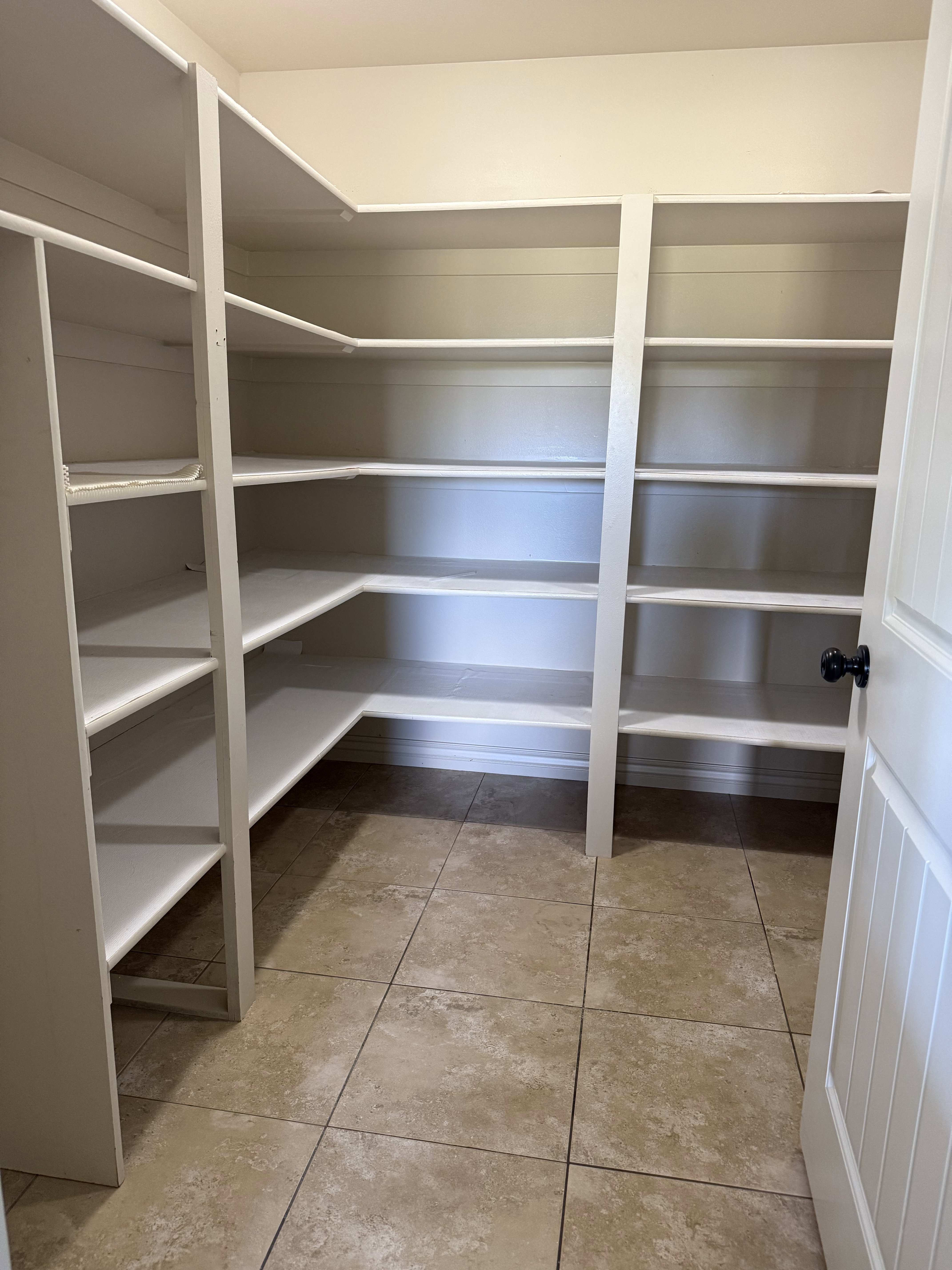 Corner pantry featuring extensive white shelving, tiled flooring, and a beadboard door with a black knob