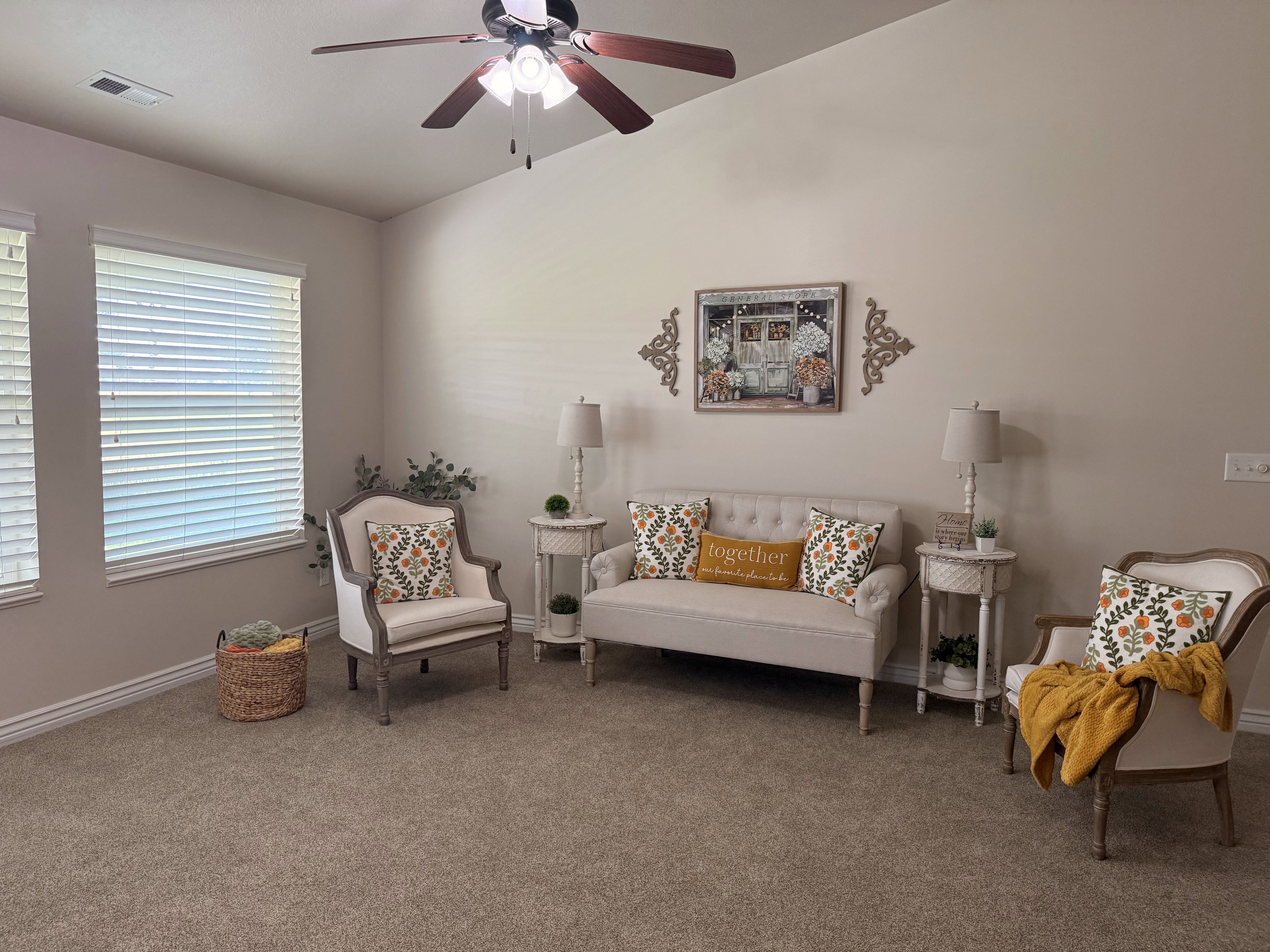 Bright living area featuring vaulted ceilings, a ceiling fan with integrated lighting, two large windows with blinds, and neutral carpeting
