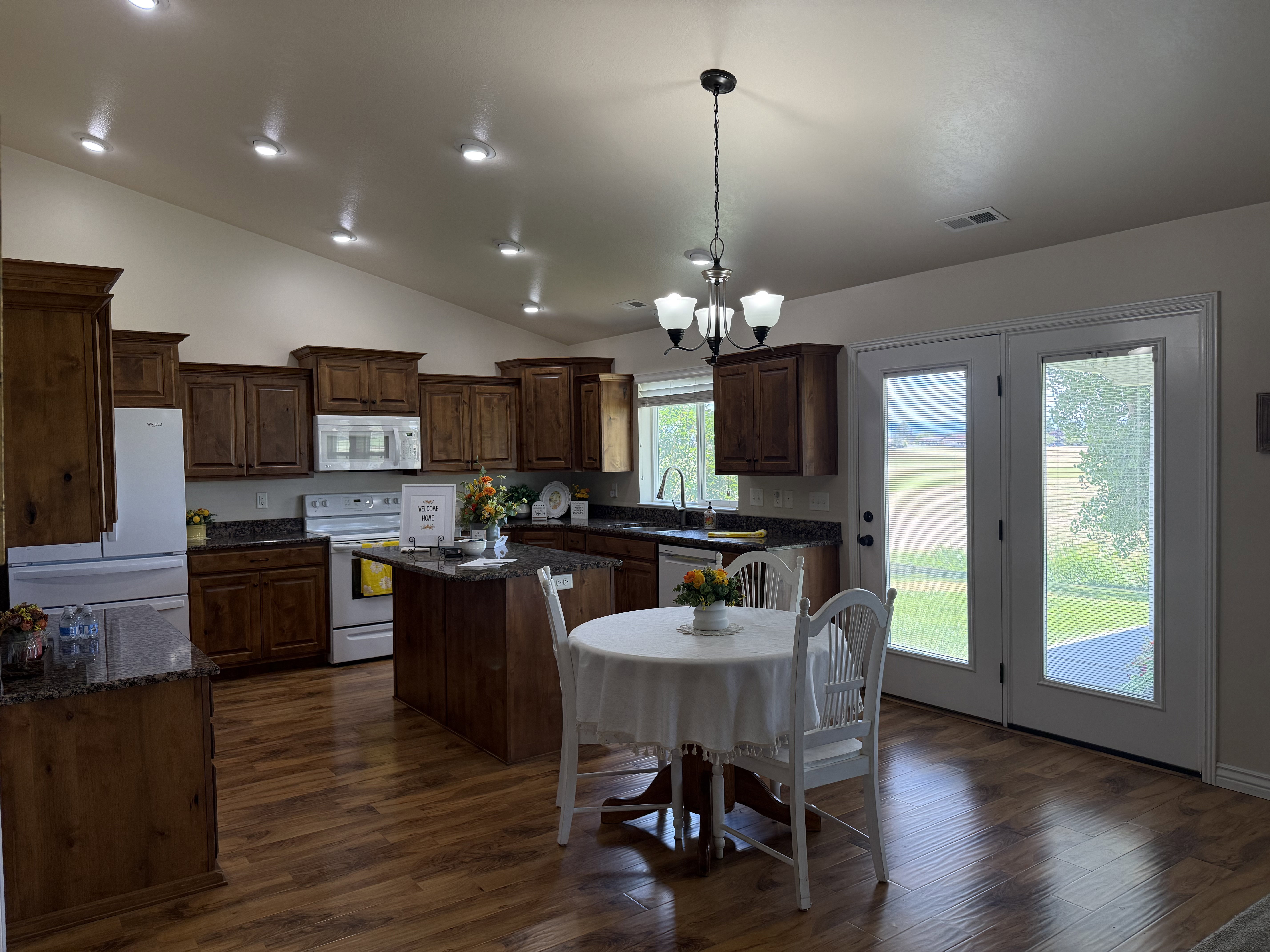 Kitchen featuring wood-finish flooring, dark wood cabinetry, granite countertops, and white appliances