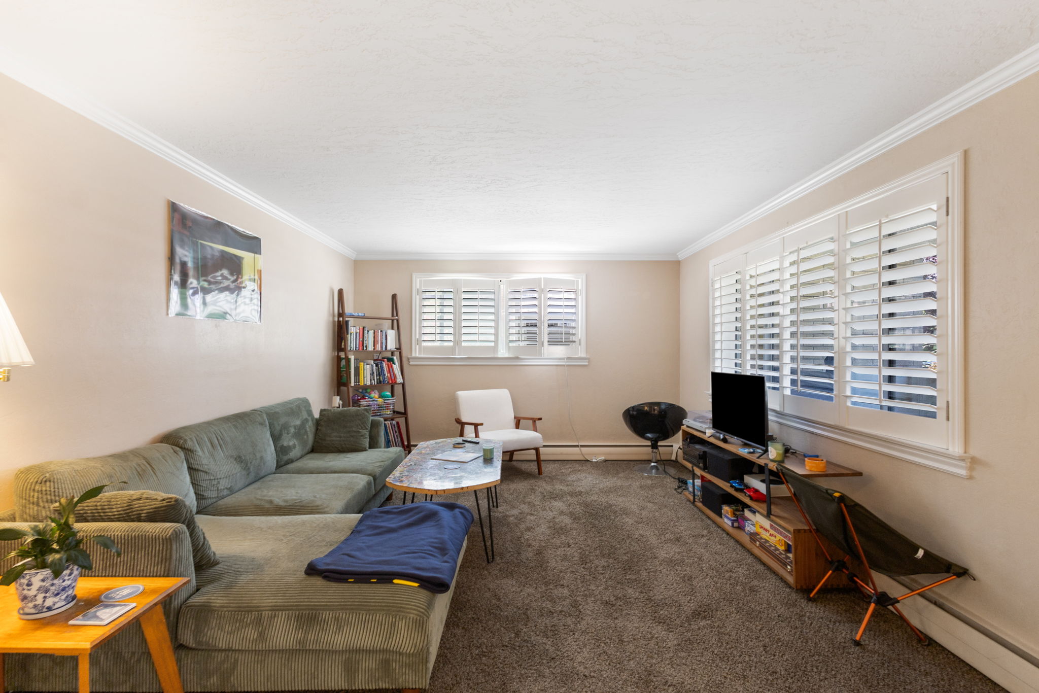 Spacious living area featuring neutral wall tones, crown molding, and plush carpeting