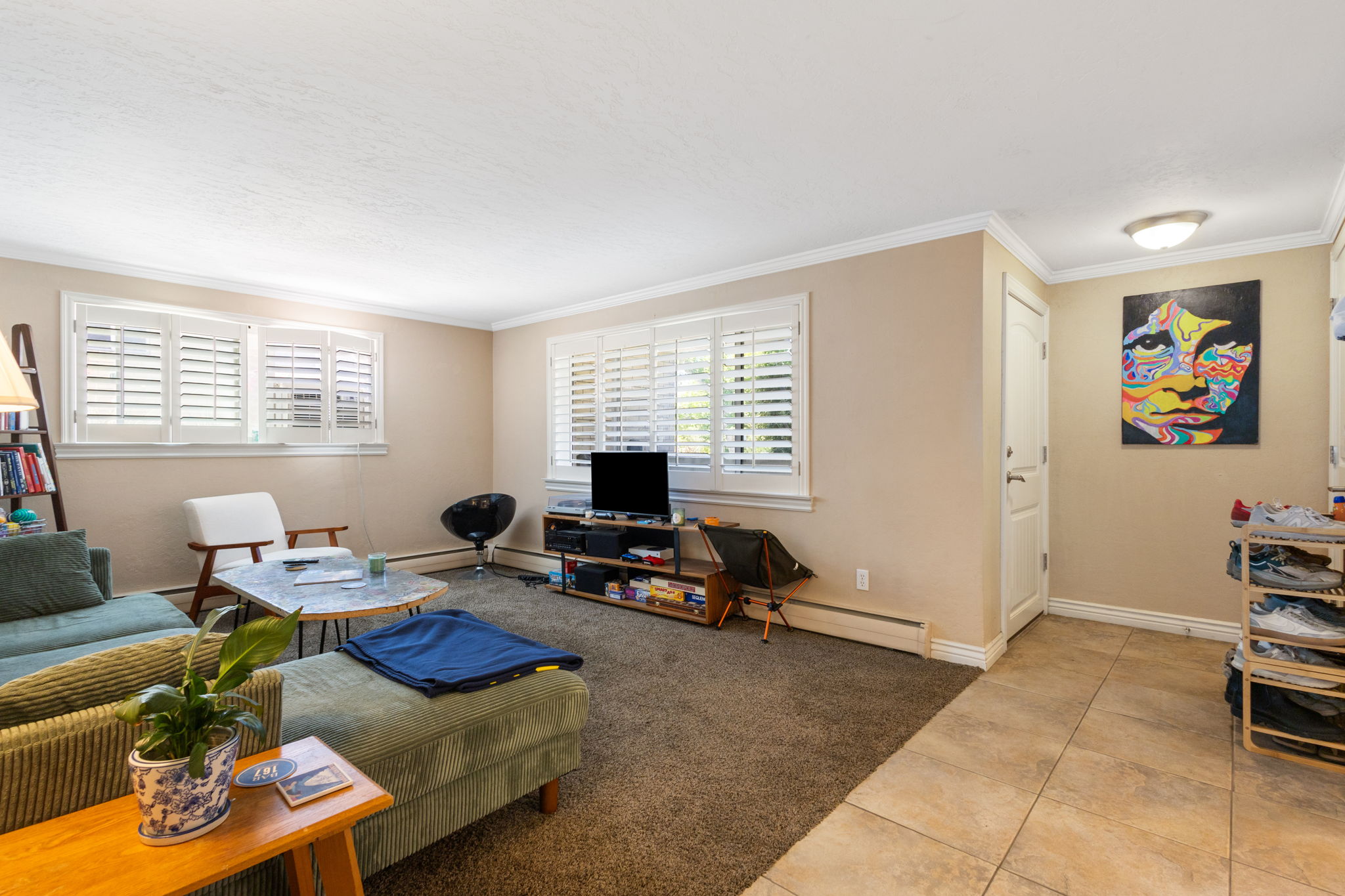 Living area featuring multiple windows with louvered shutters, crown molding, and neutral wall tones