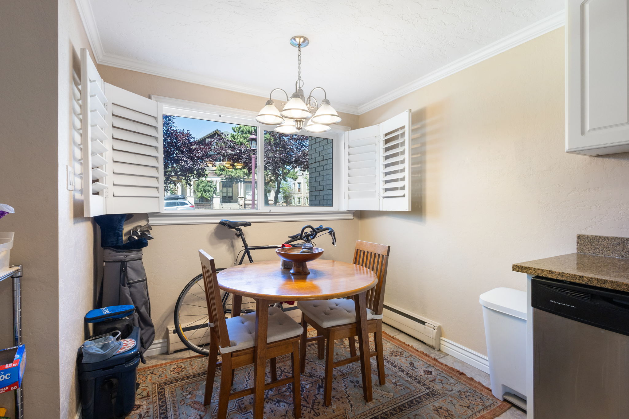 Dining area featuring a window with white plantation shutters, a multi-light pendant fixture, crown molding, and a patterned area rug