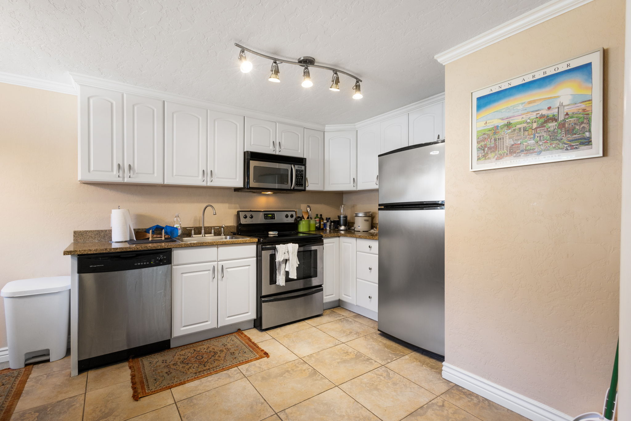Kitchen featuring white upper and lower cabinetry, stainless steel appliances, speckled countertops, and tile flooring