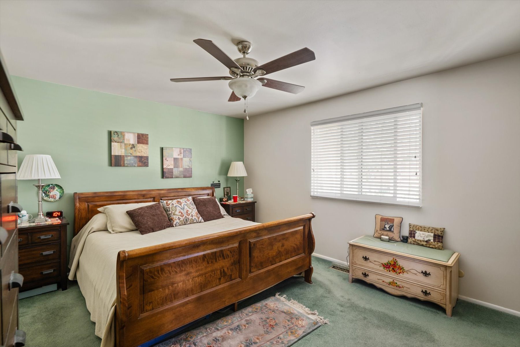 Bedroom featuring a ceiling fan, window with horizontal blinds, and a green accent wall