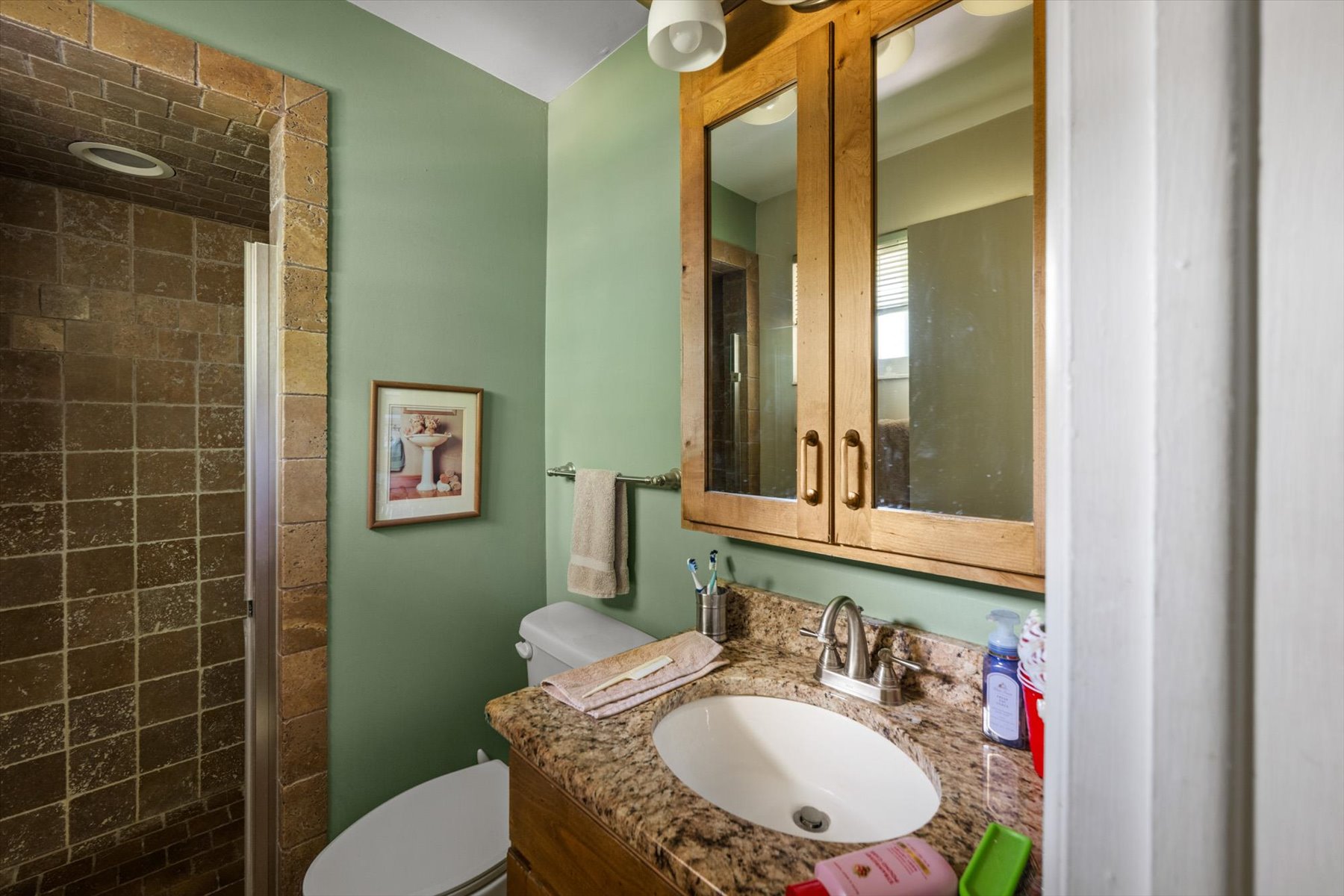 Bathroom featuring a tiled shower enclosure, vanity with a granite-finish countertop, undermount sink, and wood-finish mirrored medicine cabinet