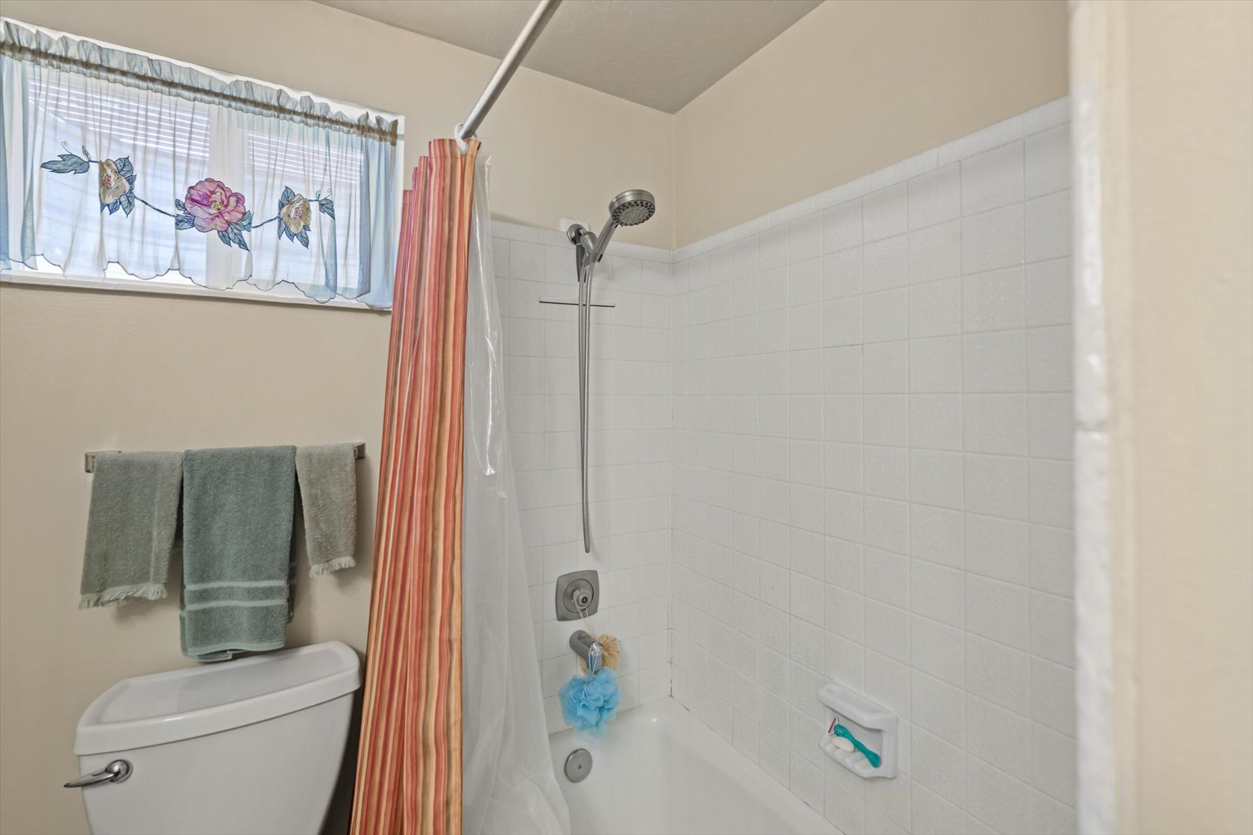 Bathtub and shower combination featuring white tiled walls and a handheld shower fixture