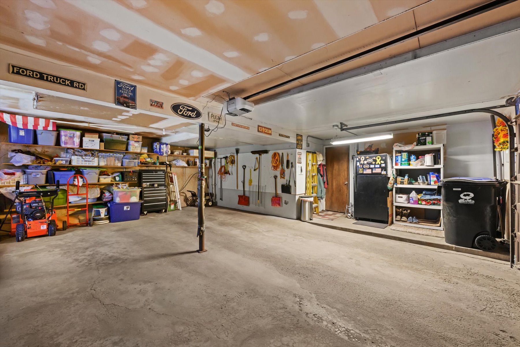 Spacious garage with concrete flooring, fluorescent lighting, and extensive wall shelving