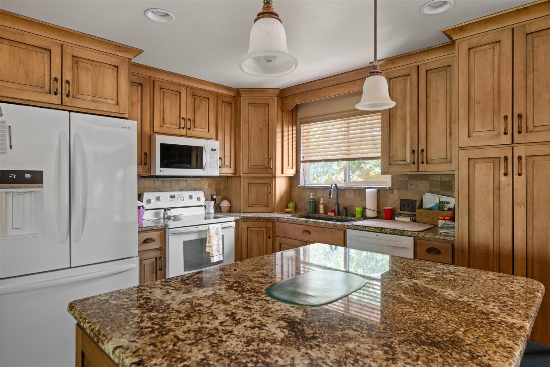 Kitchen featuring a large island with a stone-finish countertop, extensive wood cabinetry, white appliances, a tile backsplash, and recessed and pendant lighting